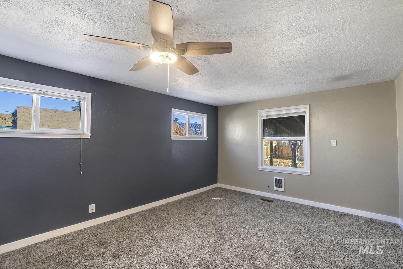 Carpeted empty room featuring a textured ceiling and ceiling fan