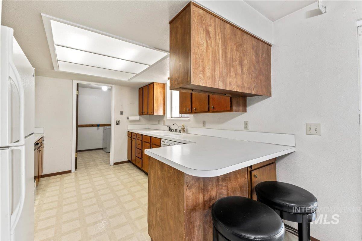 Kitchen with brown cabinets, light floors, a peninsula, a kitchen breakfast bar, and freestanding refrigerator