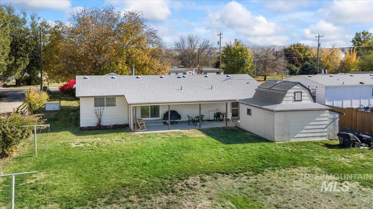 Rear view of property with a patio area, roof with shingles, and an outbuilding
