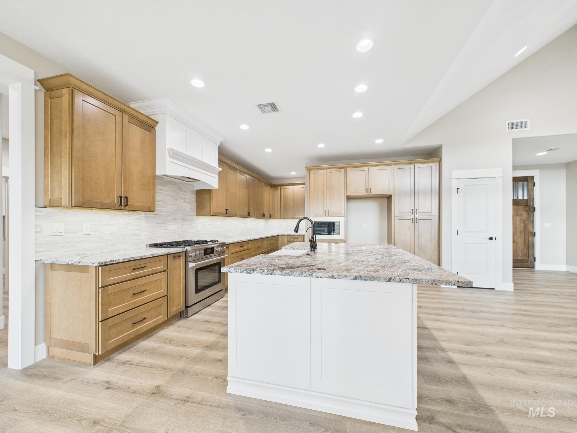 Kitchen with high end stainless steel range oven, light stone counters, light wood finished floors, recessed lighting, and a kitchen island with sink