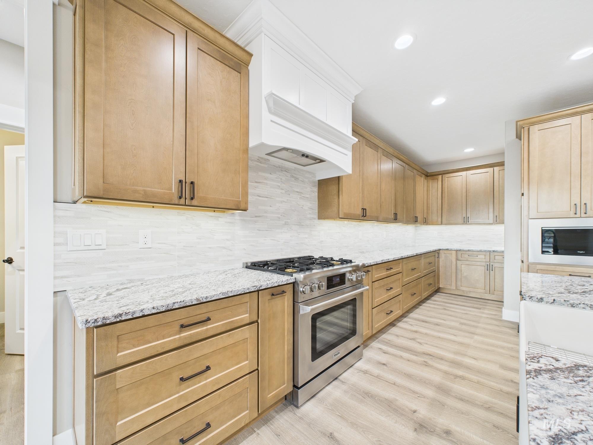 Kitchen with stainless steel range with gas stovetop, recessed lighting, light stone countertops, tasteful backsplash, and light wood-style flooring