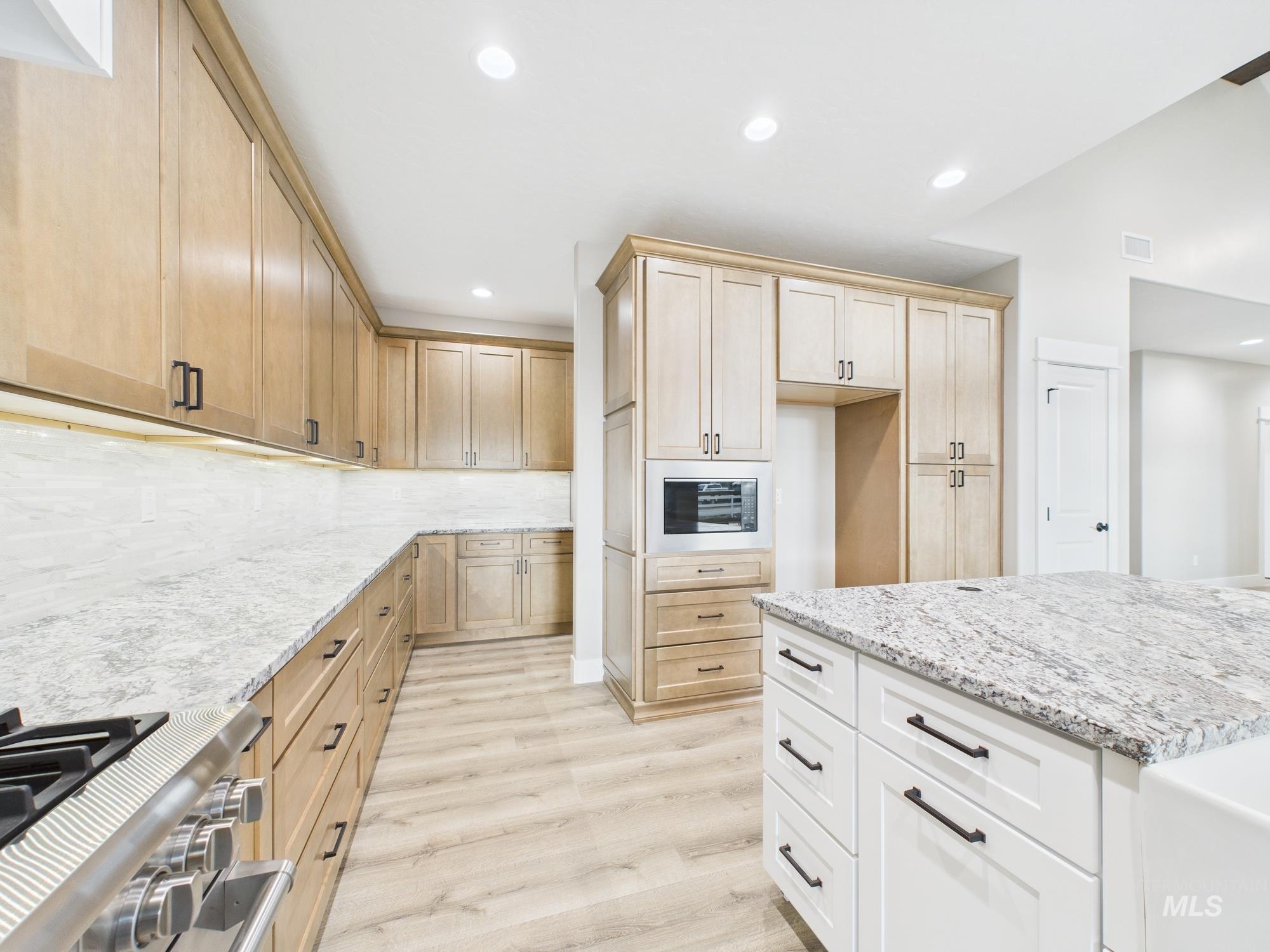 Kitchen featuring light brown cabinets, light stone counters, light wood finished floors, stove, and recessed lighting