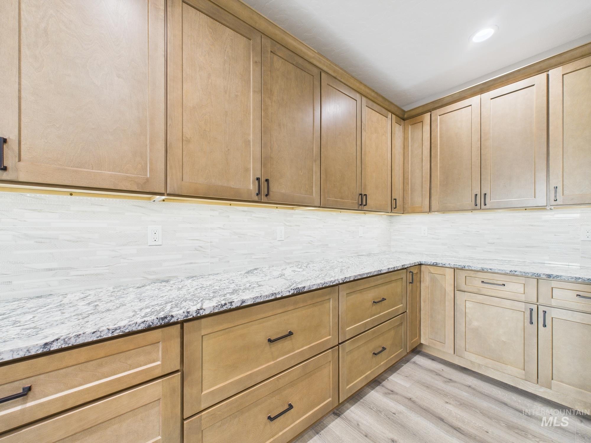 Kitchen featuring light wood-style floors, backsplash, and light stone countertops