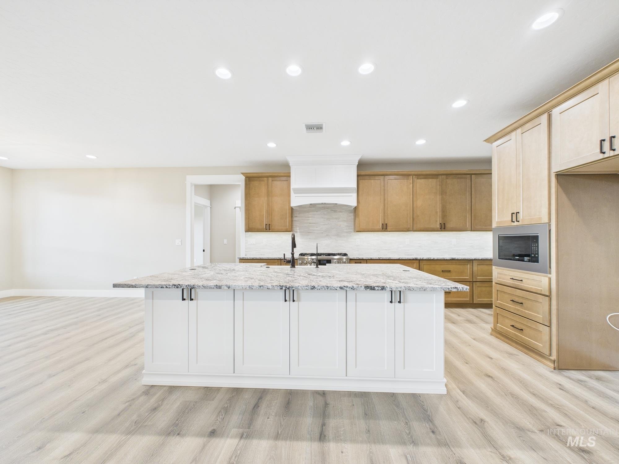 Kitchen featuring recessed lighting, backsplash, a kitchen island with sink, light stone countertops, and built in microwave