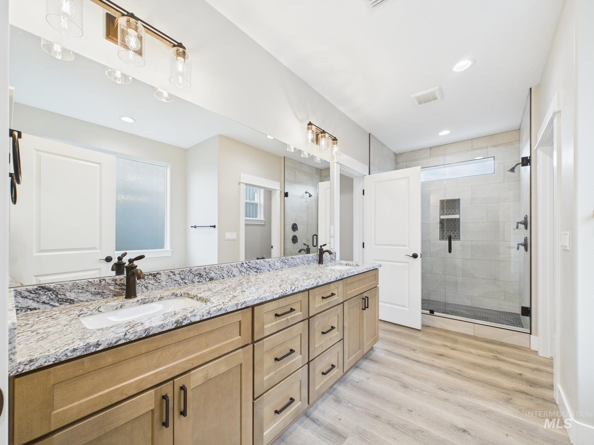 Bathroom featuring double vanity, recessed lighting, a shower stall, and wood finished floors