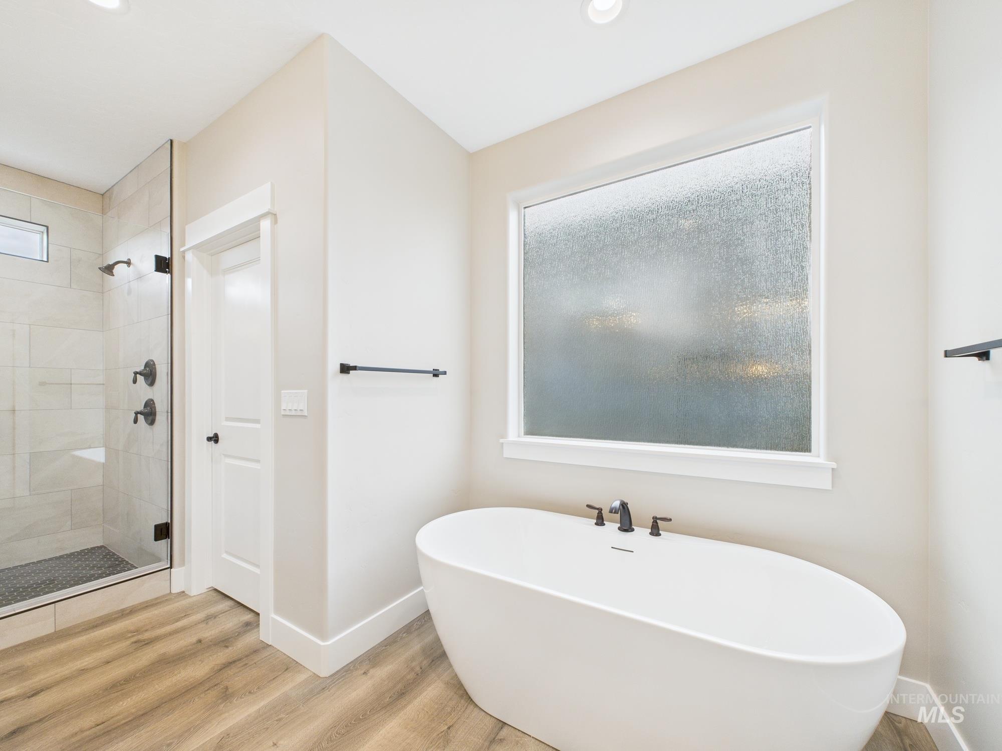 Full bathroom featuring wood finished floors, a freestanding bath, a stall shower, and recessed lighting