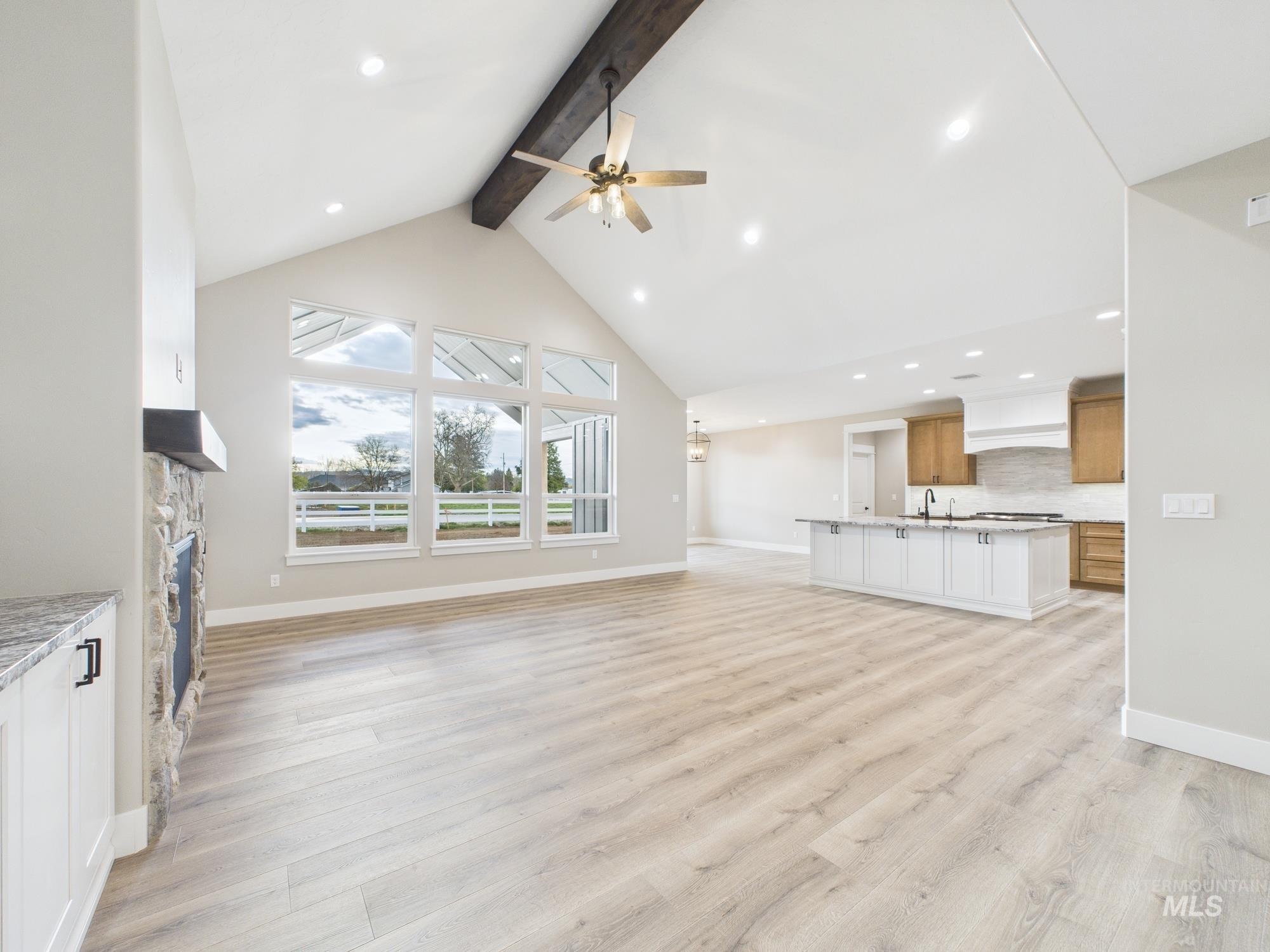 Unfurnished living room featuring beam ceiling, high vaulted ceiling, light wood-type flooring, ceiling fan, and a fireplace