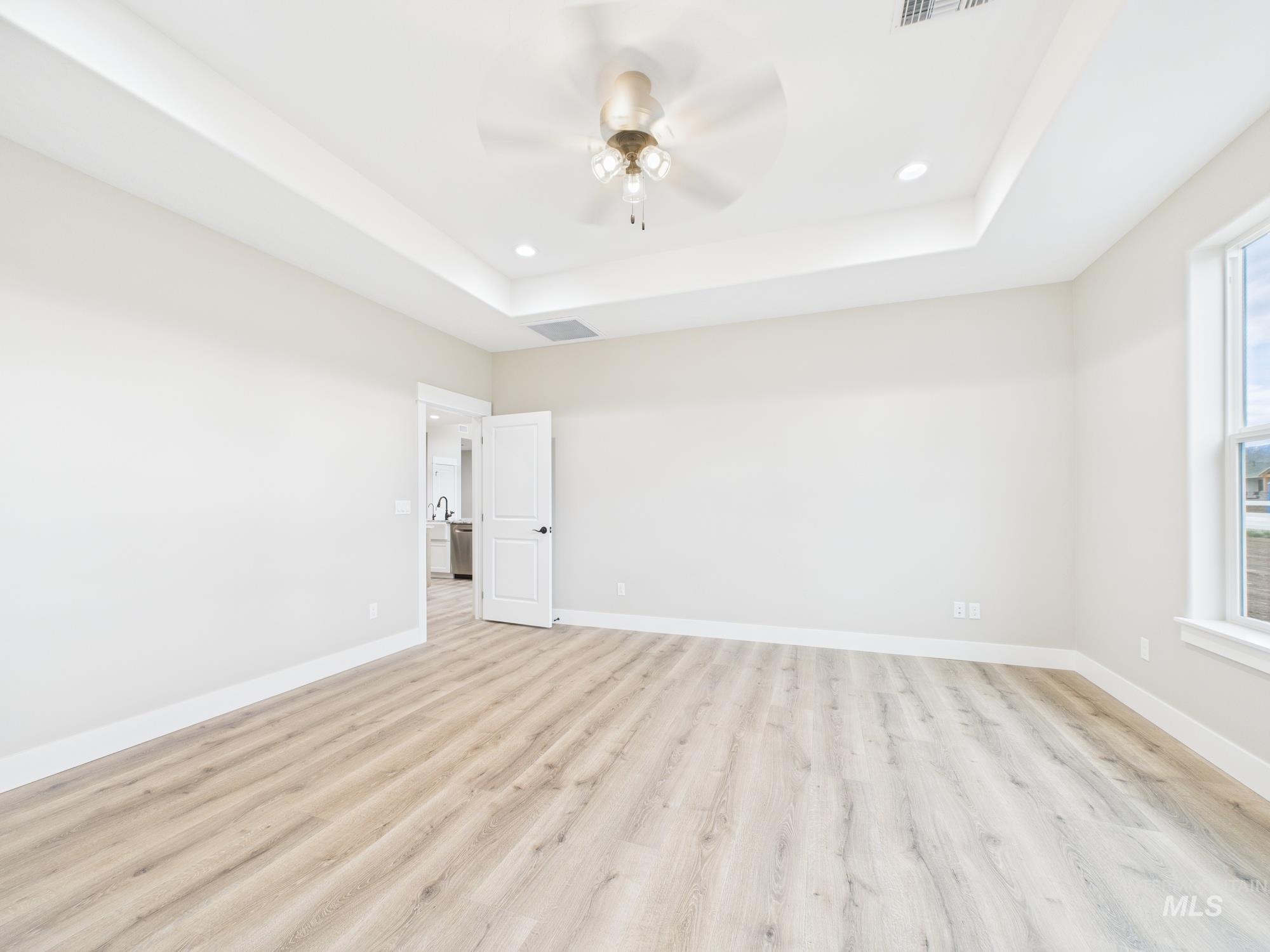 Empty room with recessed lighting, light wood-type flooring, a raised ceiling, and ceiling fan