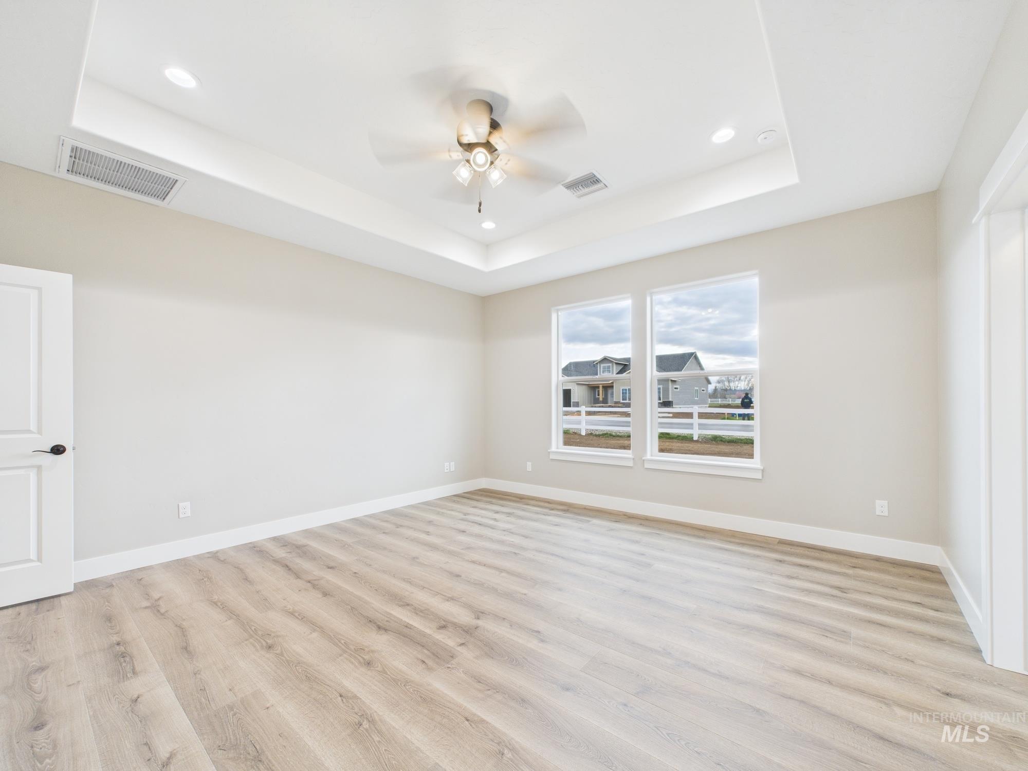 Empty room with a tray ceiling, light wood finished floors, recessed lighting, and ceiling fan