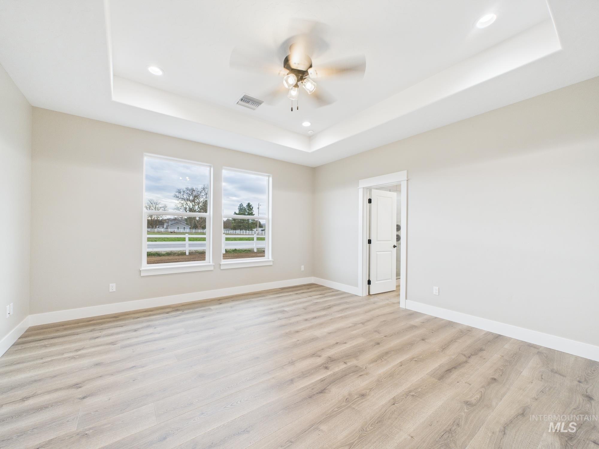 Empty room with a raised ceiling, light wood finished floors, recessed lighting, and ceiling fan