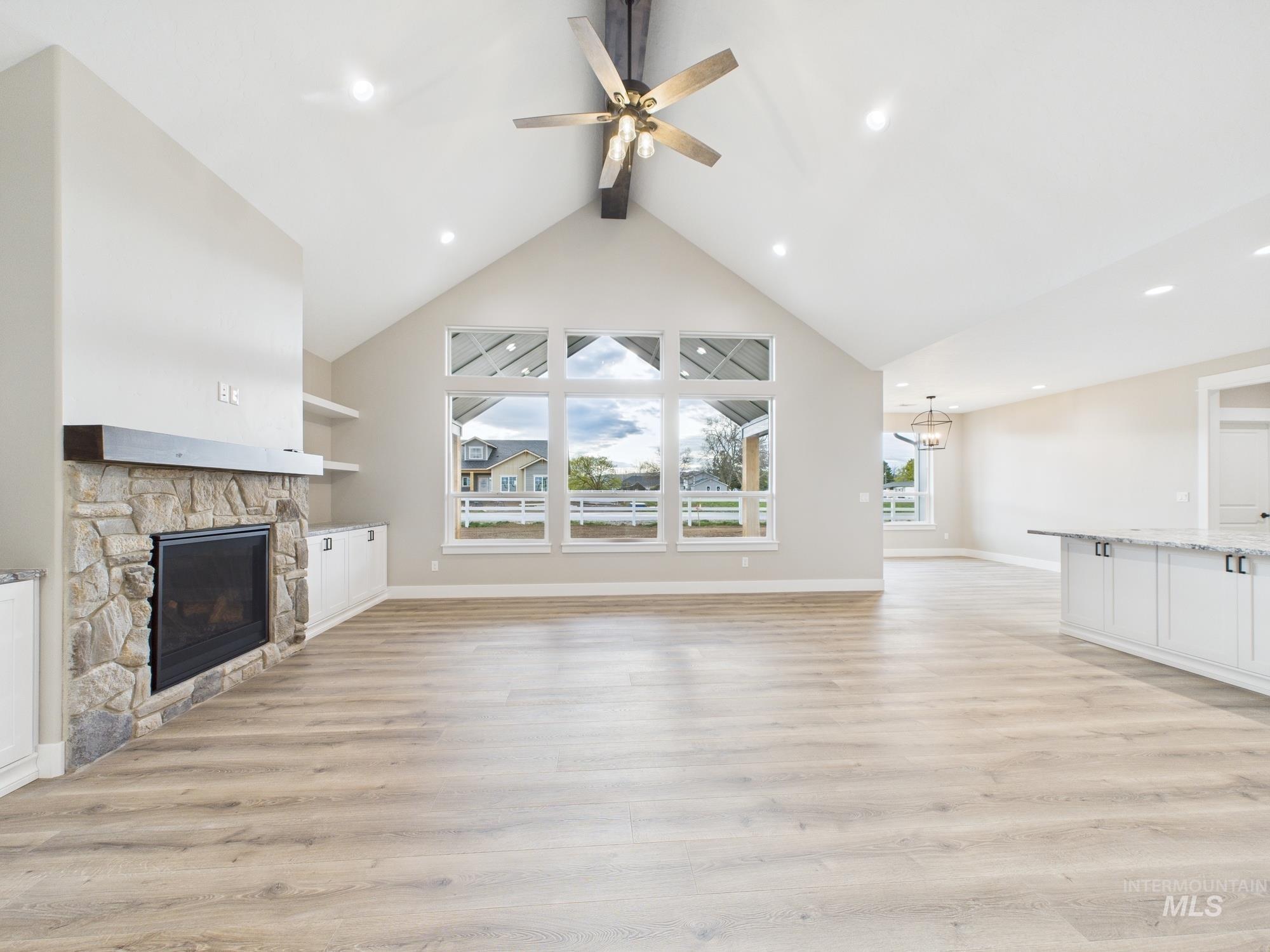 Unfurnished living room featuring beamed ceiling, light wood-style flooring, a stone fireplace, high vaulted ceiling, and recessed lighting