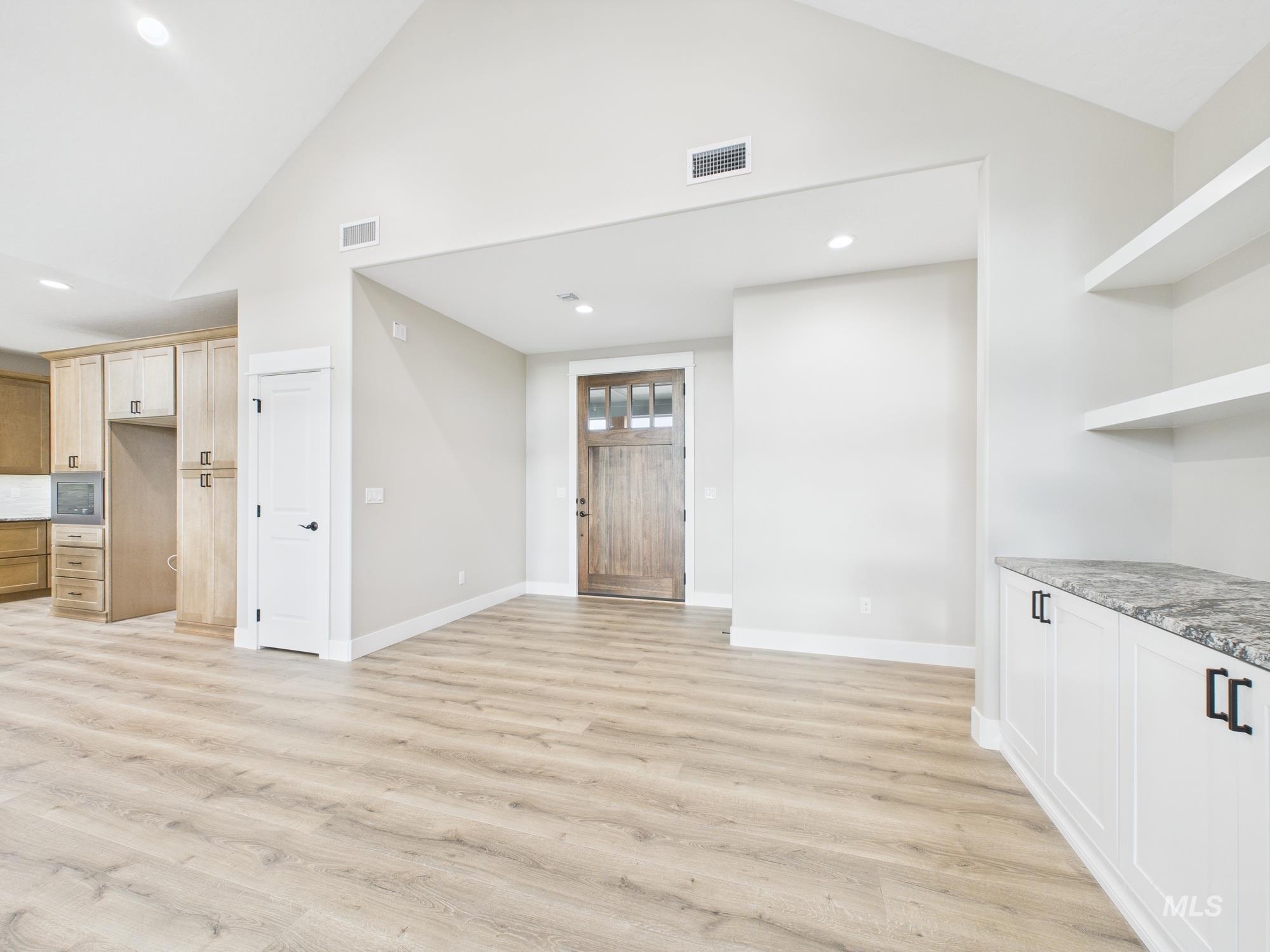 Kitchen featuring light wood-style floors, recessed lighting, high vaulted ceiling, open shelves, and light stone countertops