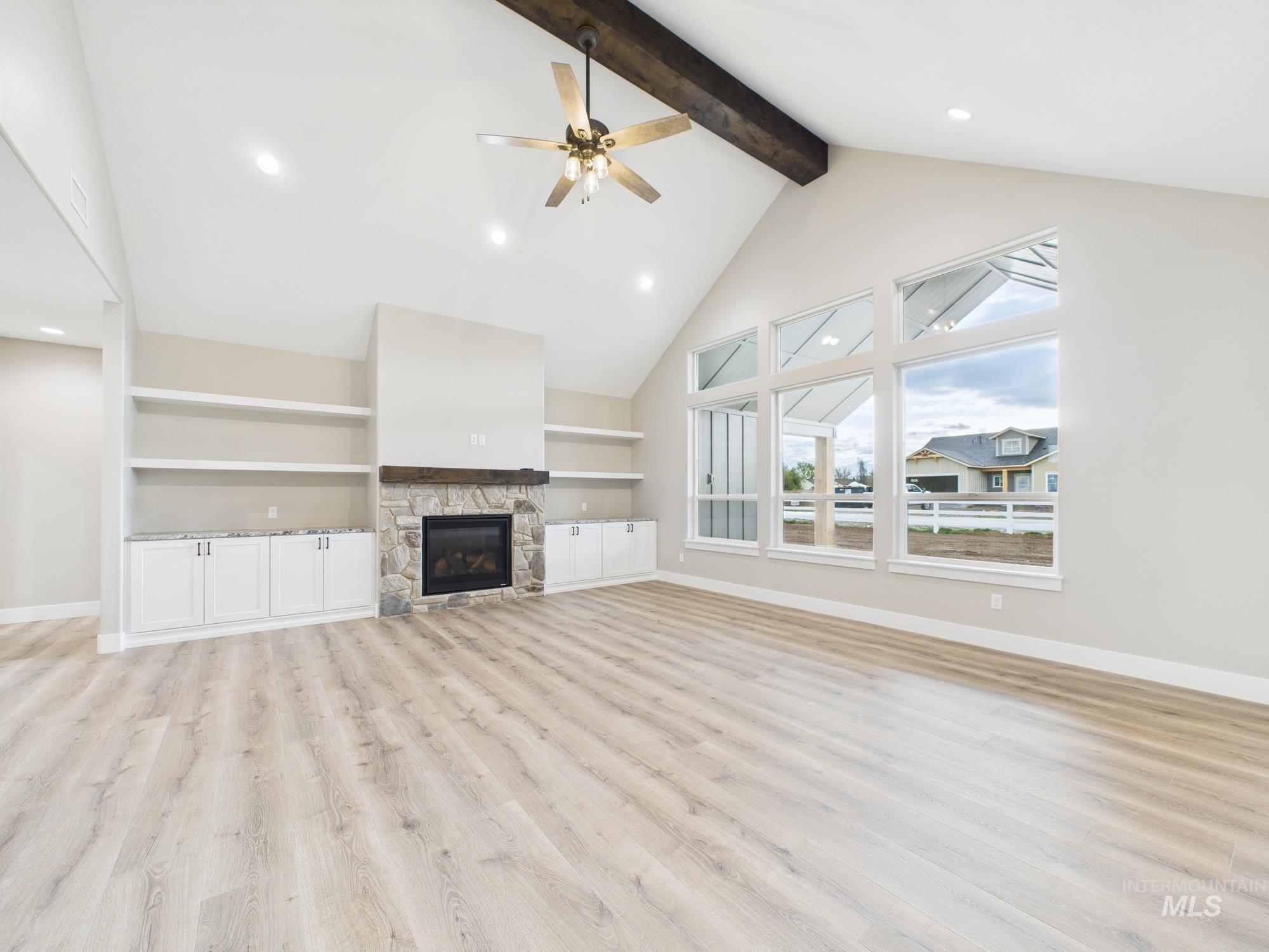 Unfurnished living room with high vaulted ceiling, beam ceiling, light wood-type flooring, built in features, and ceiling fan