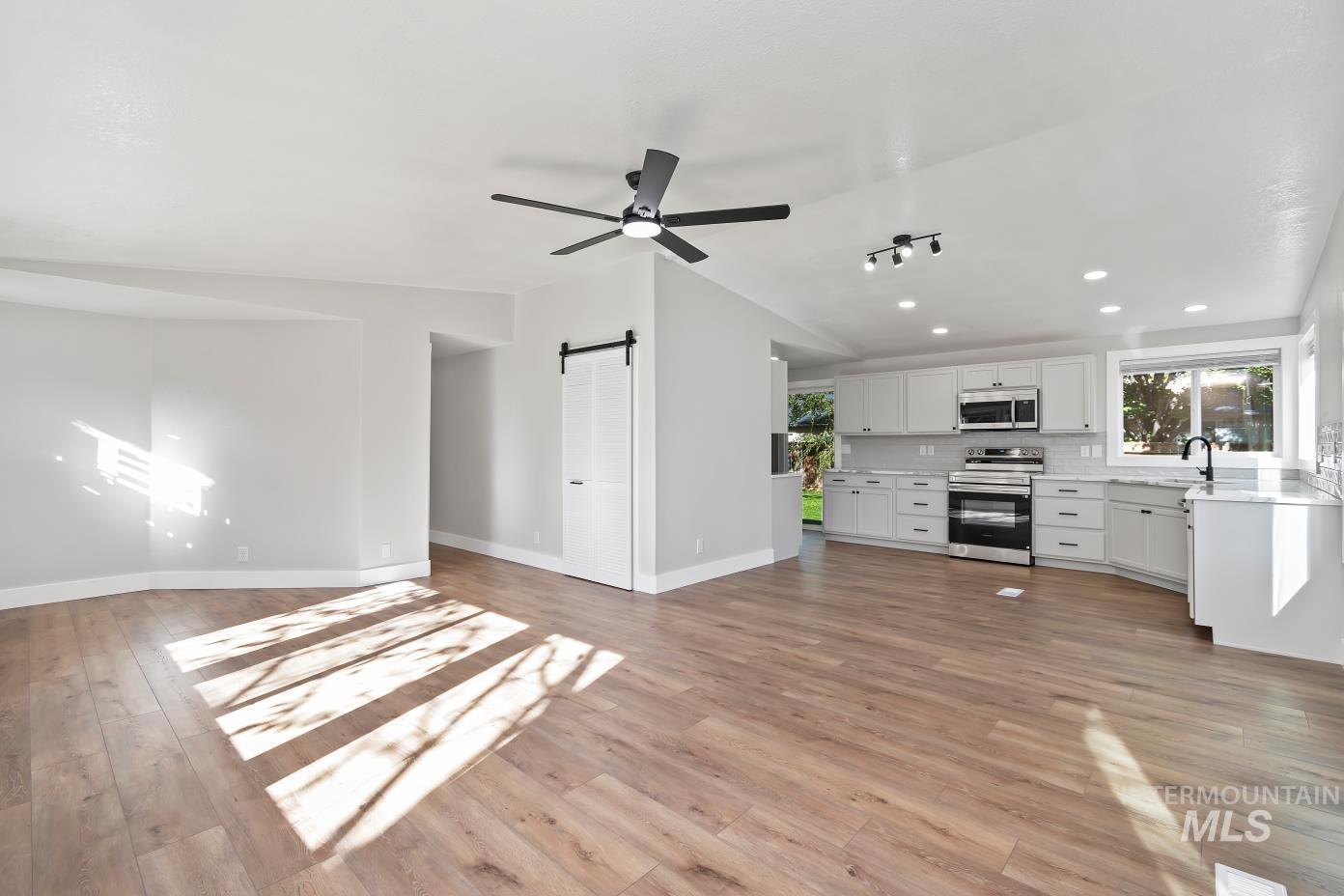 Unfurnished living room with a barn door, ceiling fan, light wood-type flooring, recessed lighting, and vaulted ceiling