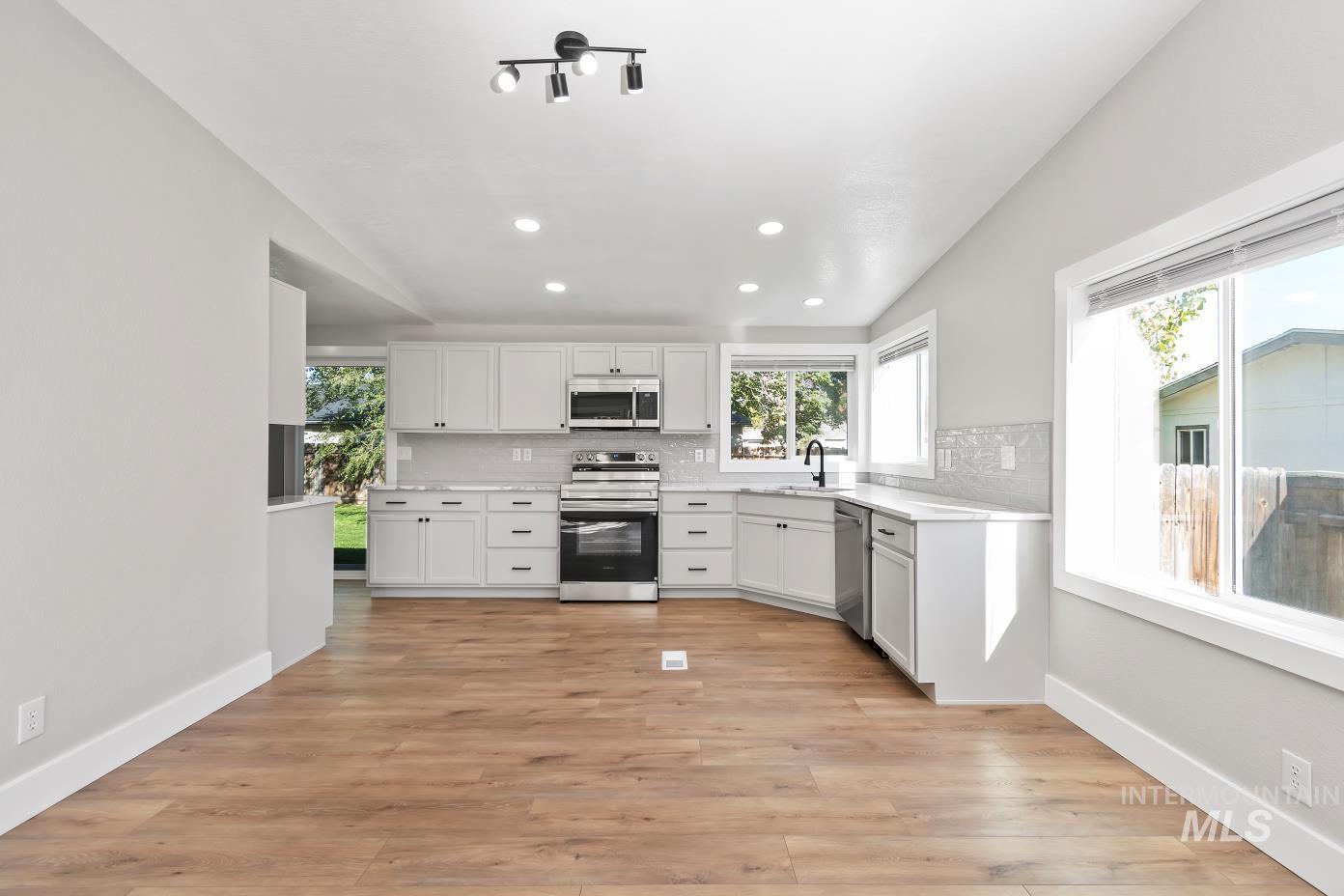 Kitchen featuring stainless steel appliances, recessed lighting, decorative backsplash, white cabinetry, and light wood finished floors