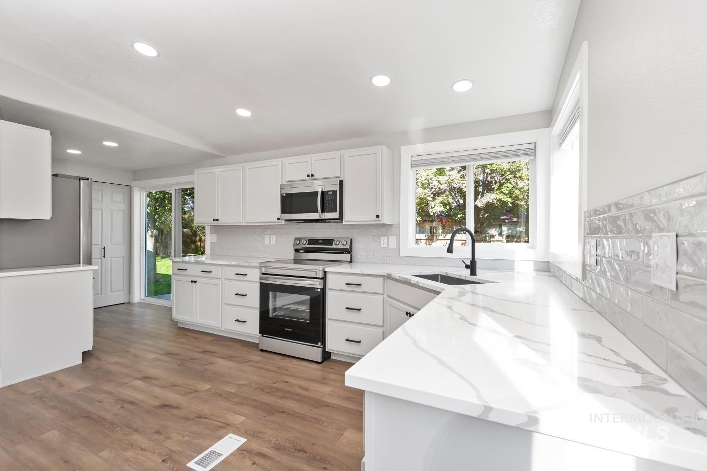 Kitchen featuring stainless steel appliances, decorative backsplash, white cabinetry, light wood-style flooring, and recessed lighting