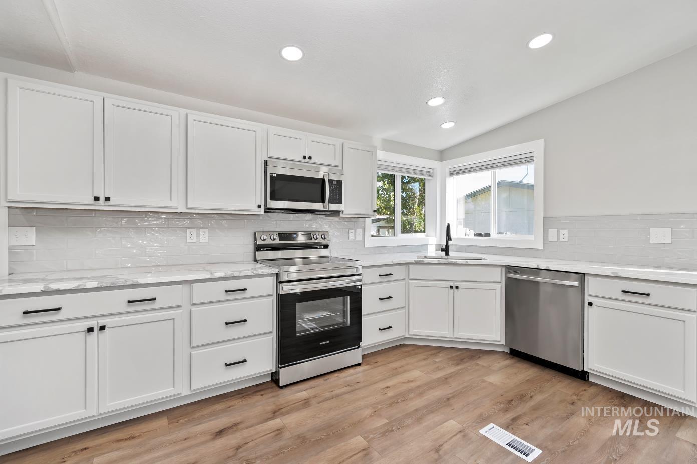 Kitchen with stainless steel appliances, decorative backsplash, recessed lighting, white cabinetry, and light wood-type flooring