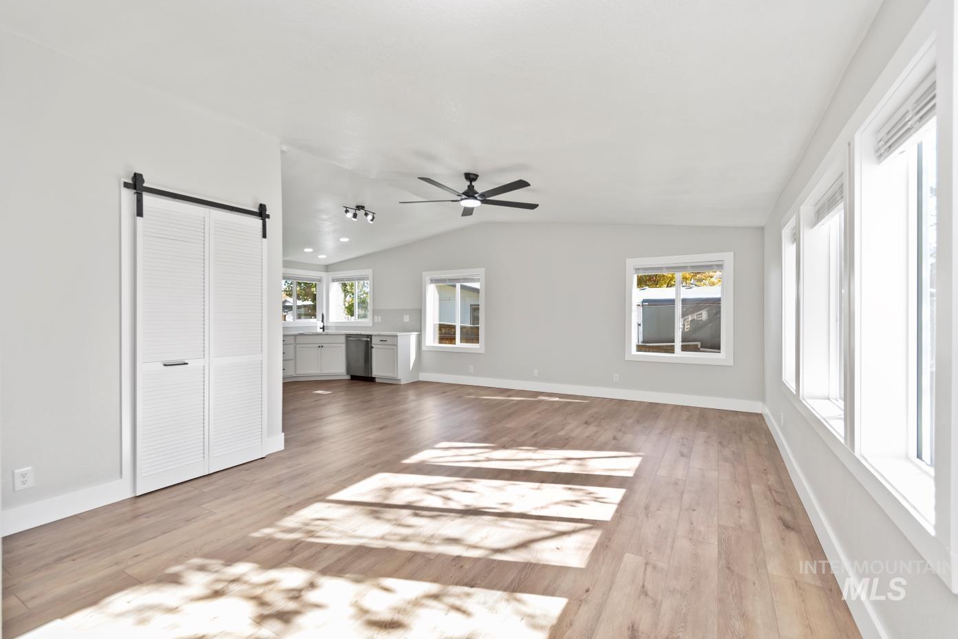 Unfurnished living room featuring a barn door, vaulted ceiling, light wood finished floors, and ceiling fan