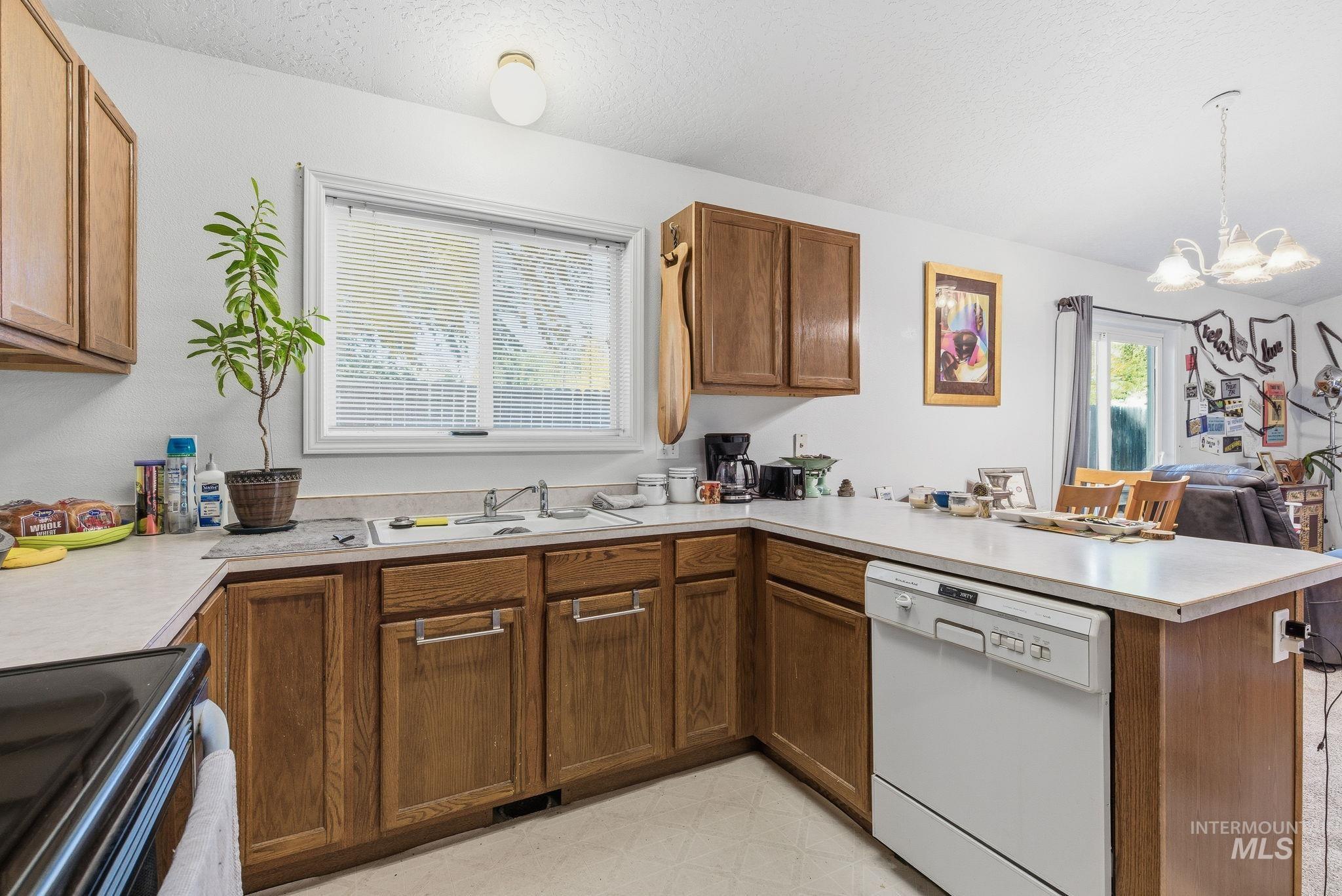Kitchen featuring a peninsula, dishwasher, range with electric cooktop, light countertops, and brown cabinetry