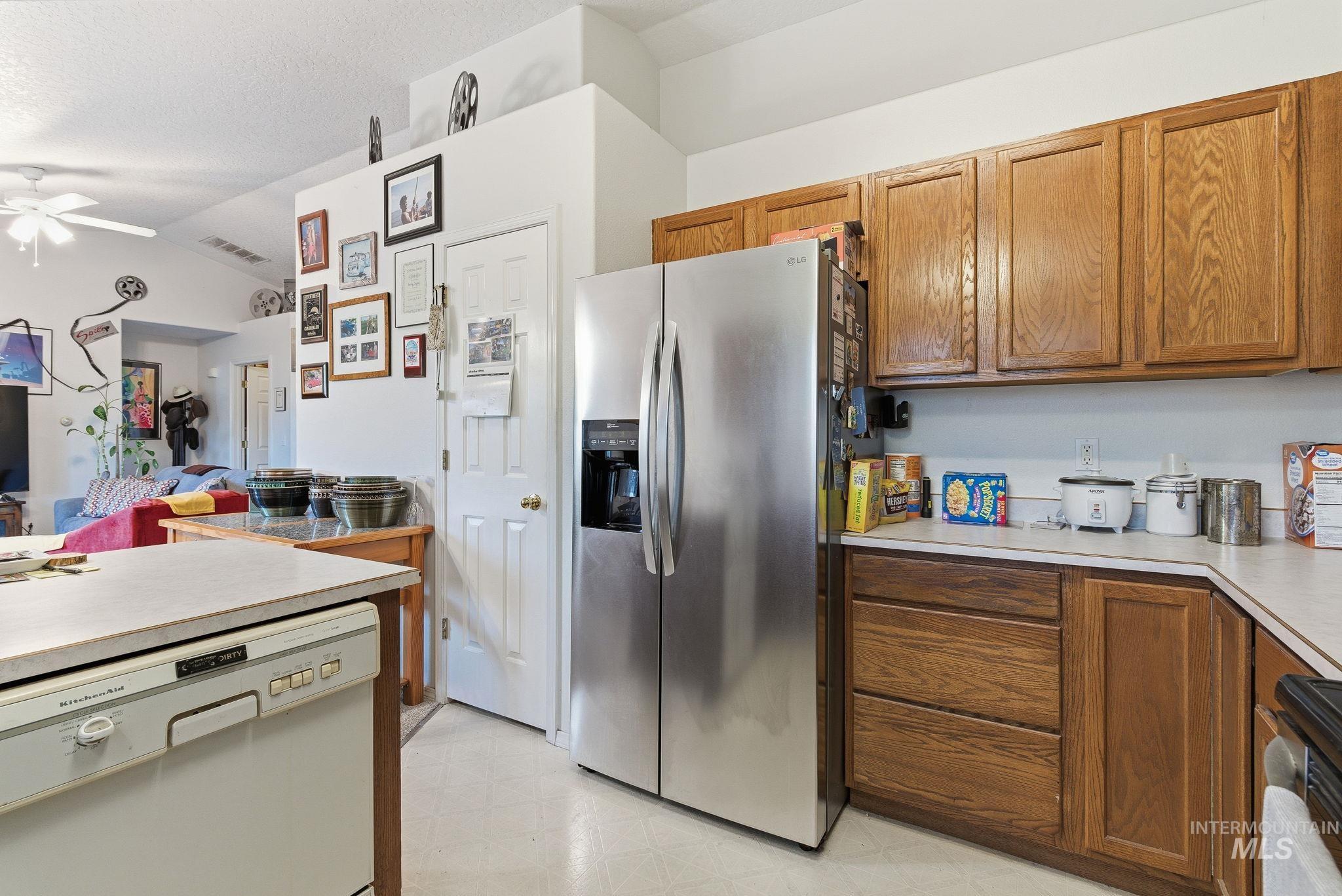 Kitchen with white dishwasher, stainless steel fridge, light countertops, brown cabinets, and vaulted ceiling