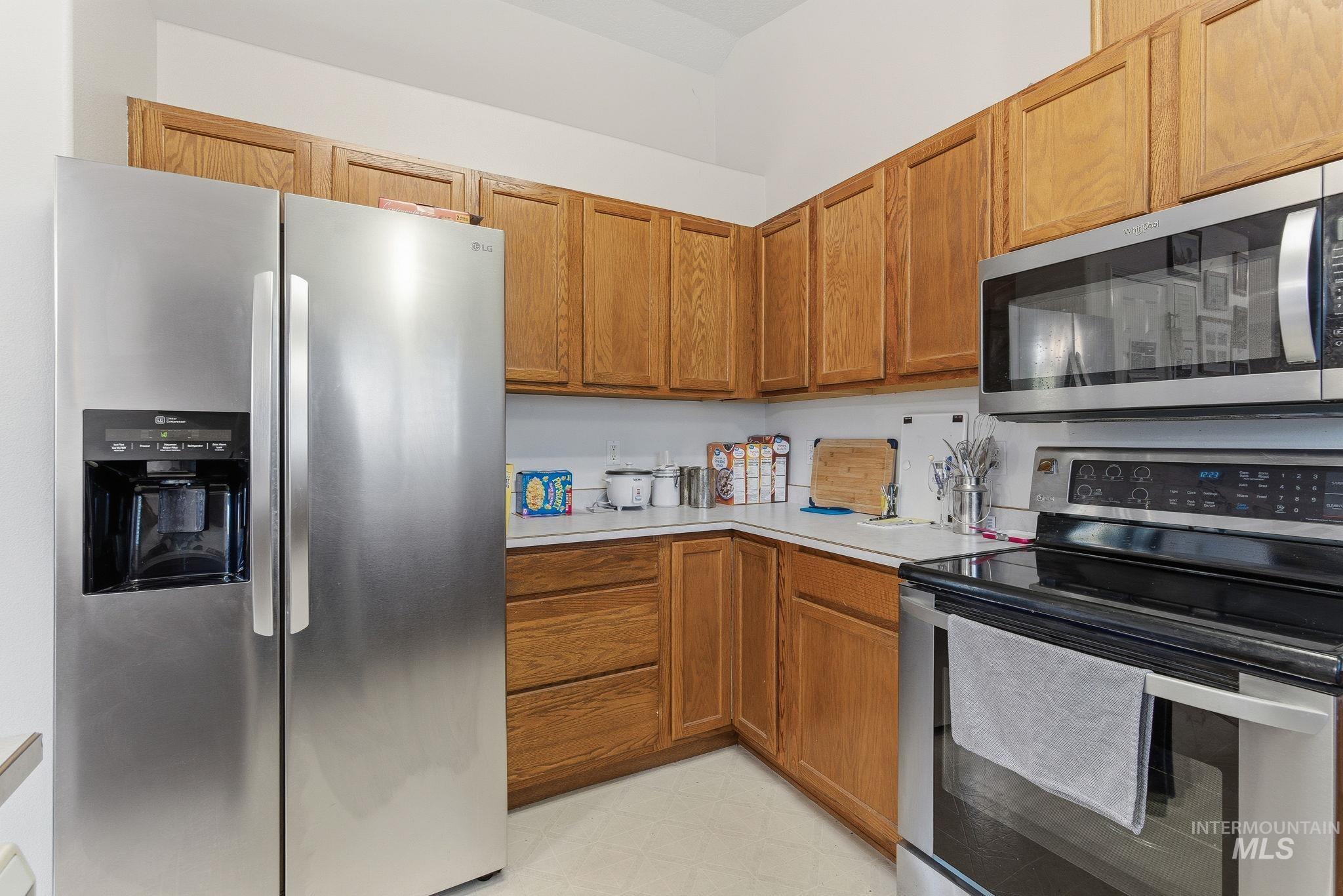 Kitchen with appliances with stainless steel finishes, light countertops, brown cabinetry, and light flooring