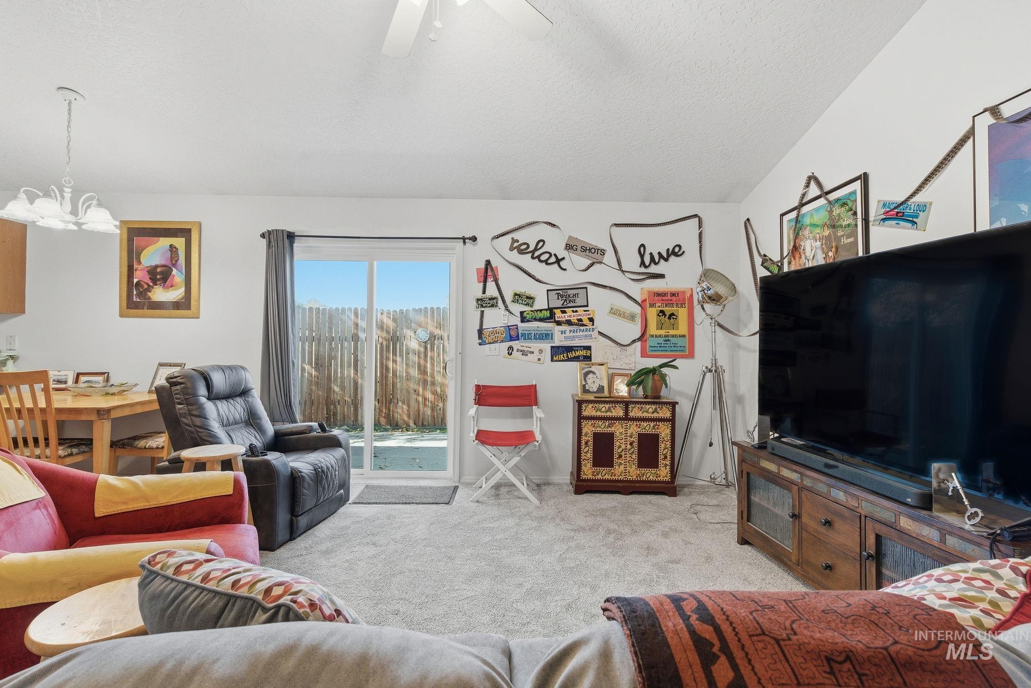 Living area with light carpet, a textured ceiling, vaulted ceiling, a chandelier, and a ceiling fan