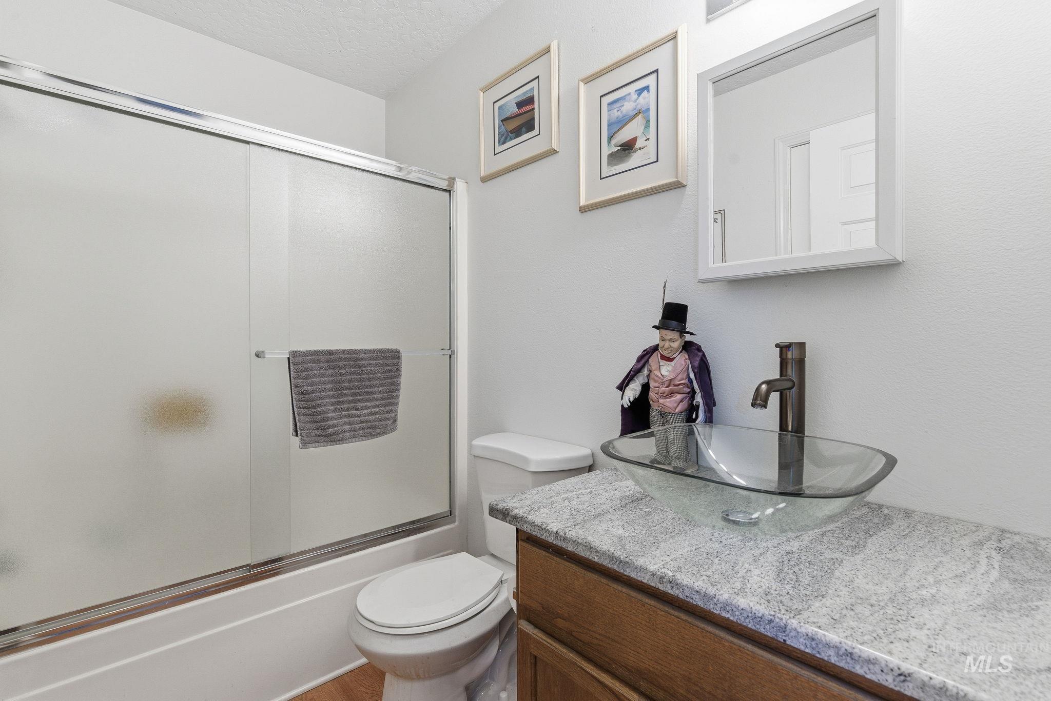 Full bathroom with vanity, shower / bath combination with glass door, and a textured ceiling
