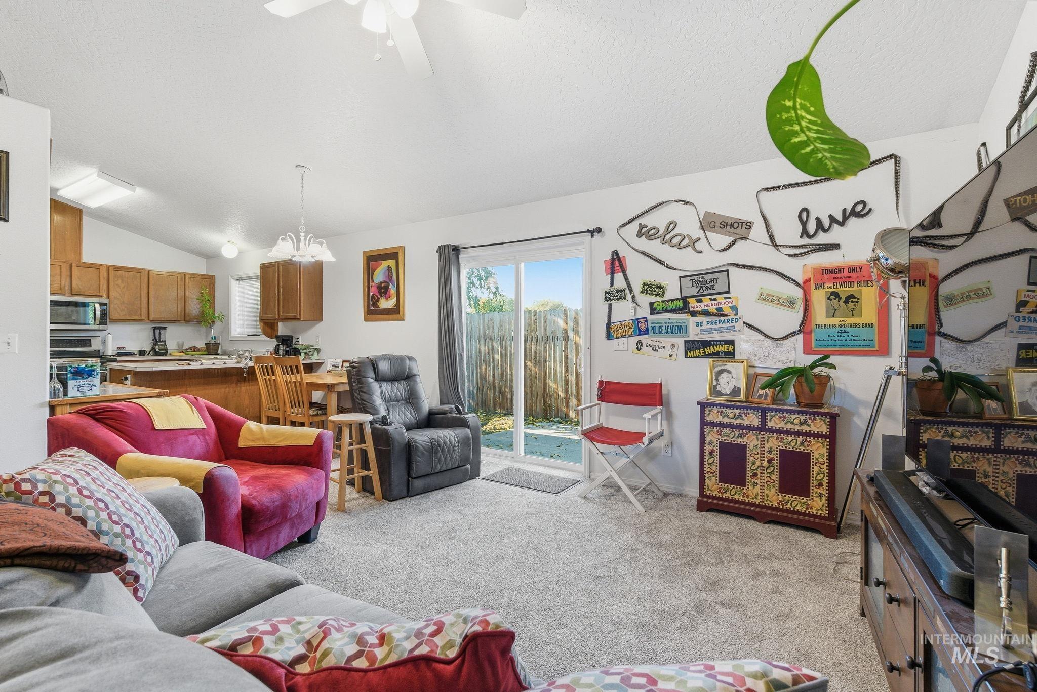 Living area featuring vaulted ceiling, light colored carpet, ceiling fan, a chandelier, and a textured ceiling