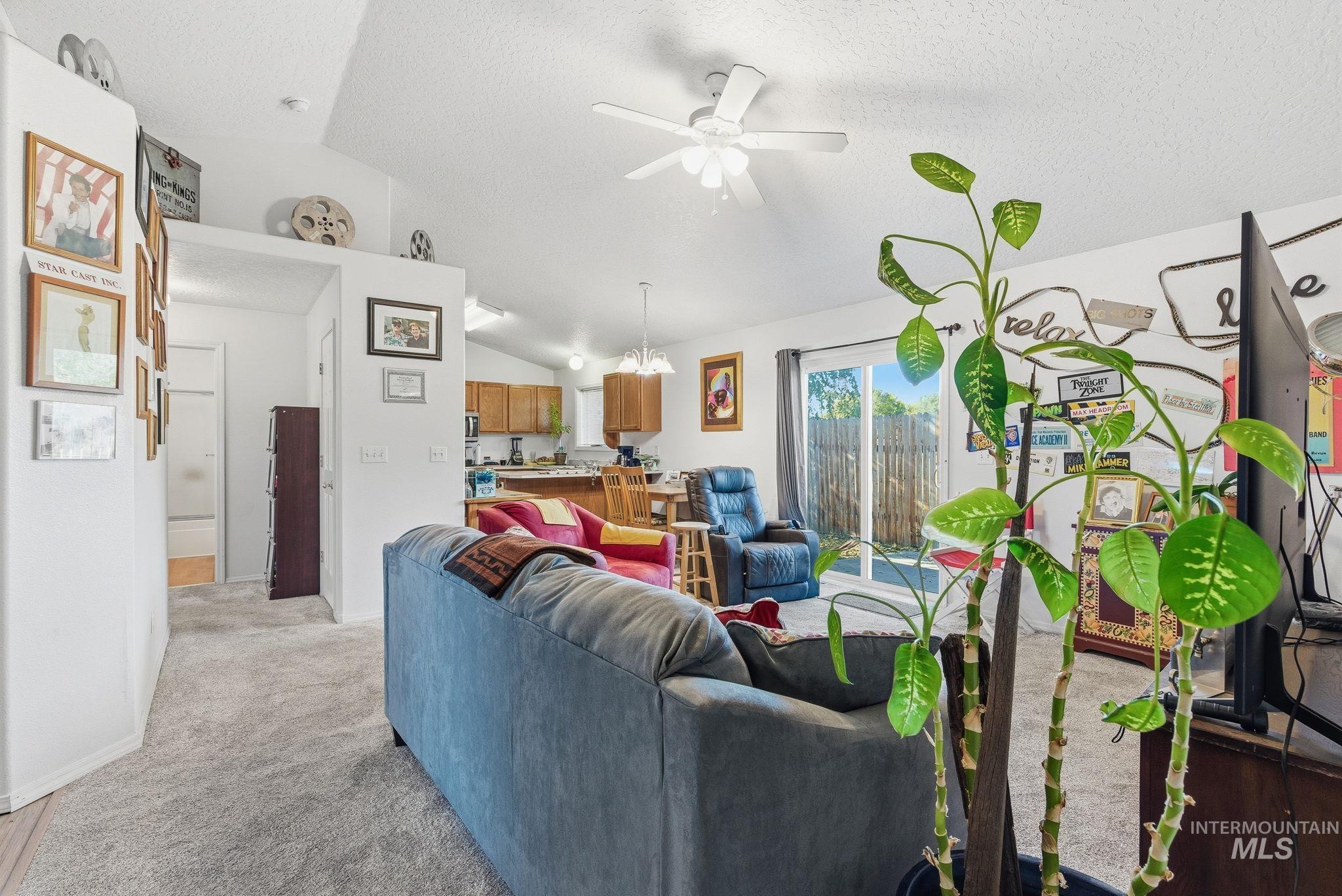 Living room with lofted ceiling, light colored carpet, ceiling fan, and a textured ceiling