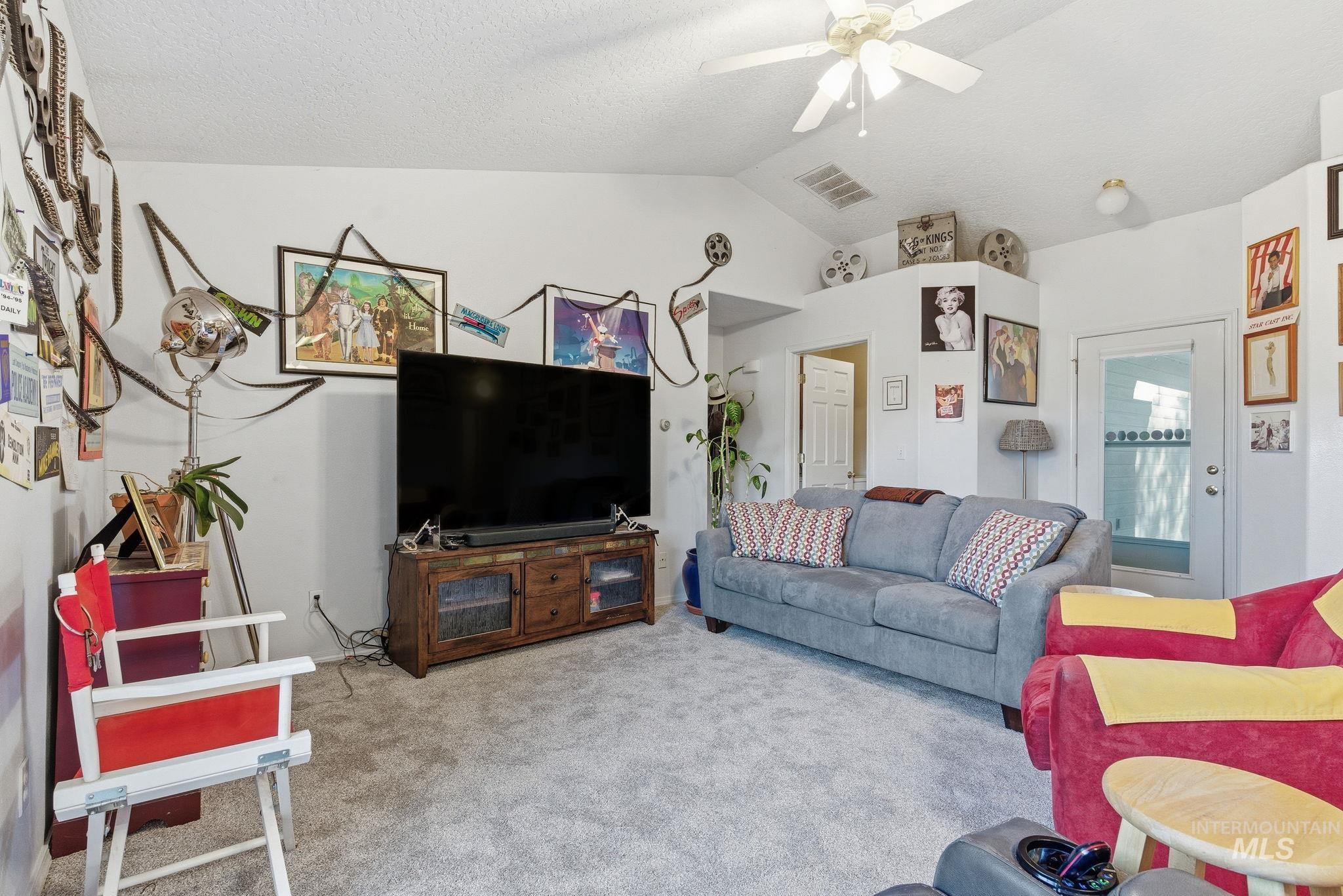 Carpeted living area with lofted ceiling, a ceiling fan, and a textured ceiling