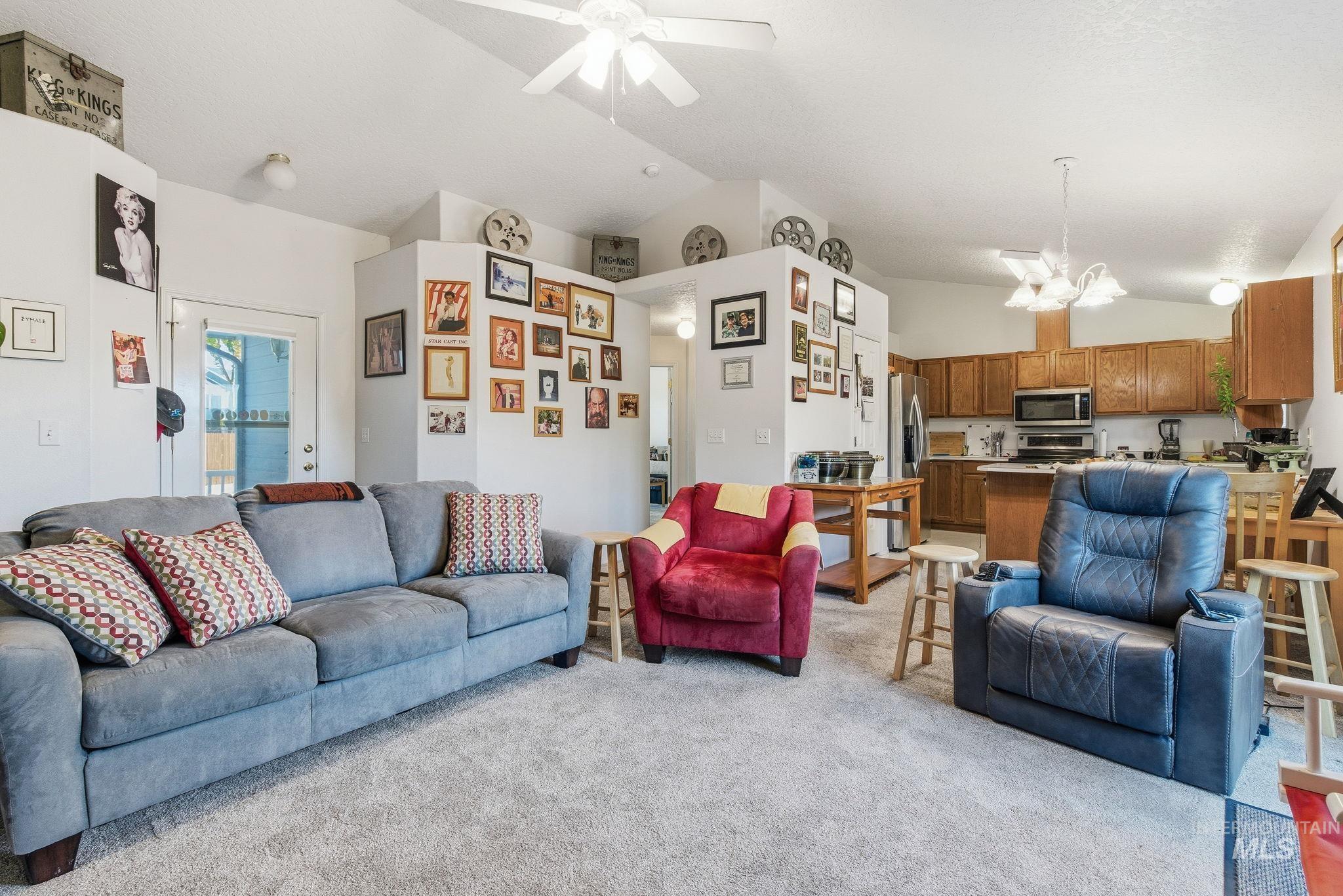 Living area with vaulted ceiling, light colored carpet, a chandelier, and a ceiling fan
