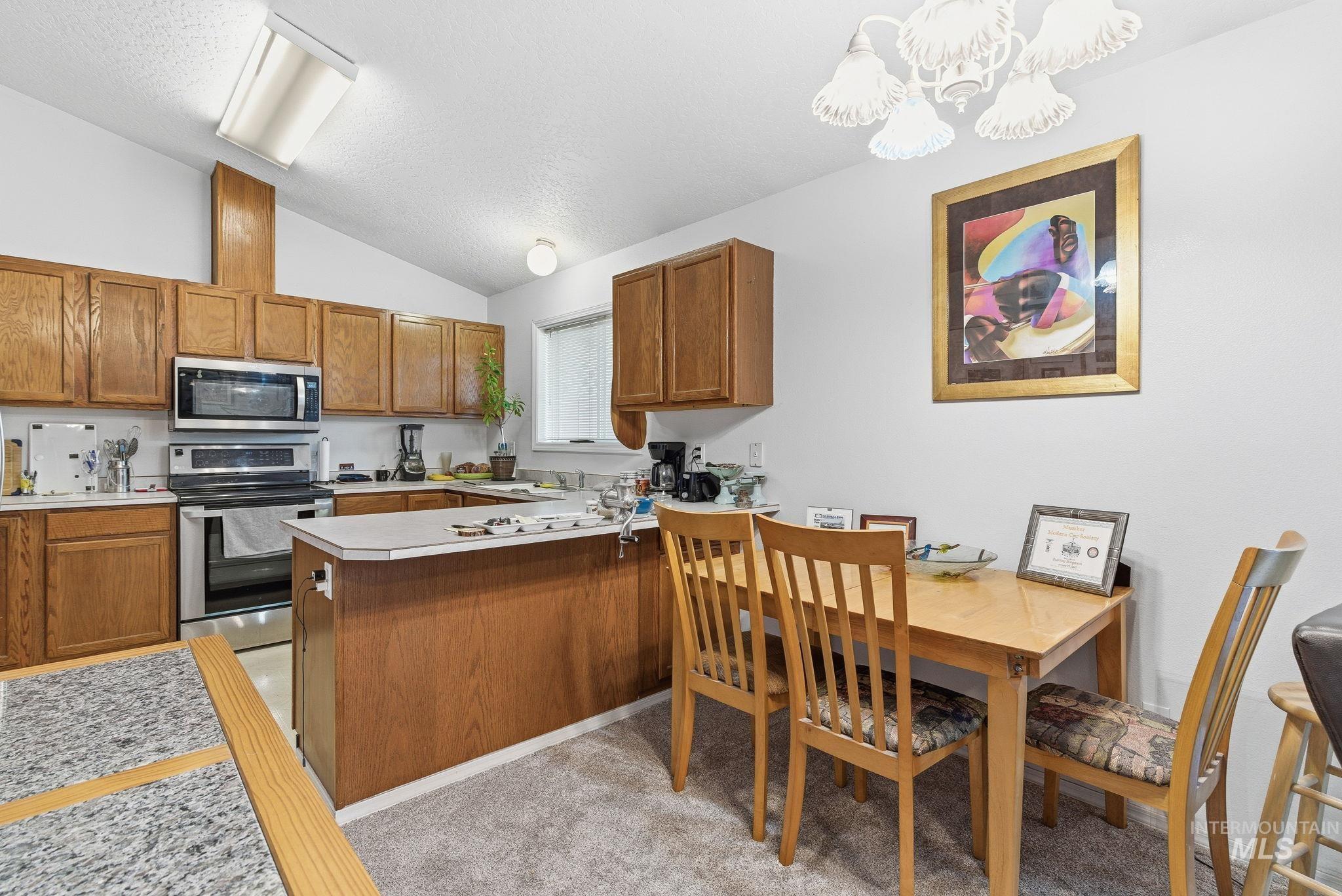 Kitchen featuring brown cabinetry, light countertops, stainless steel appliances, vaulted ceiling, and a textured ceiling