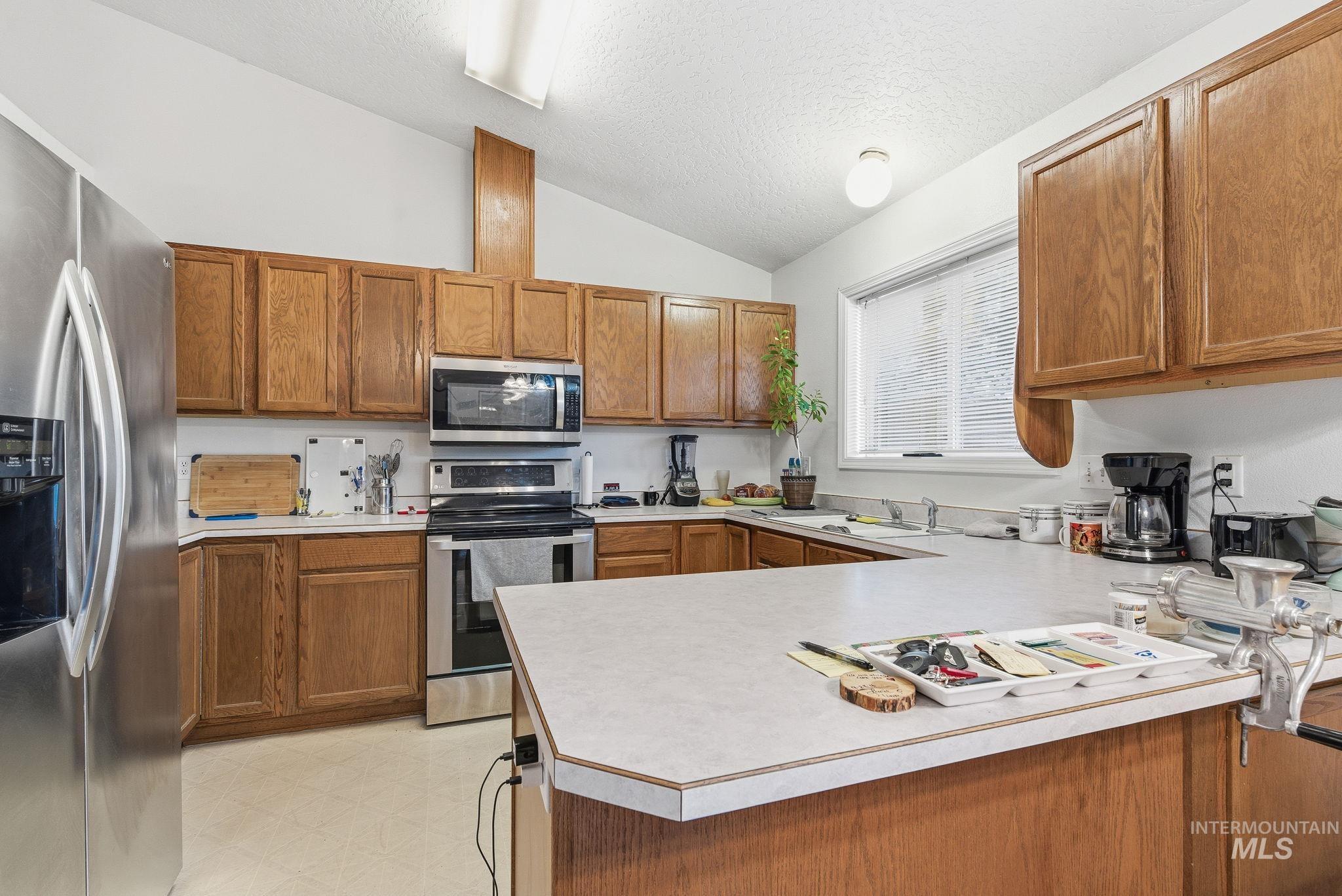 Kitchen featuring brown cabinets, light countertops, appliances with stainless steel finishes, a textured ceiling, and lofted ceiling