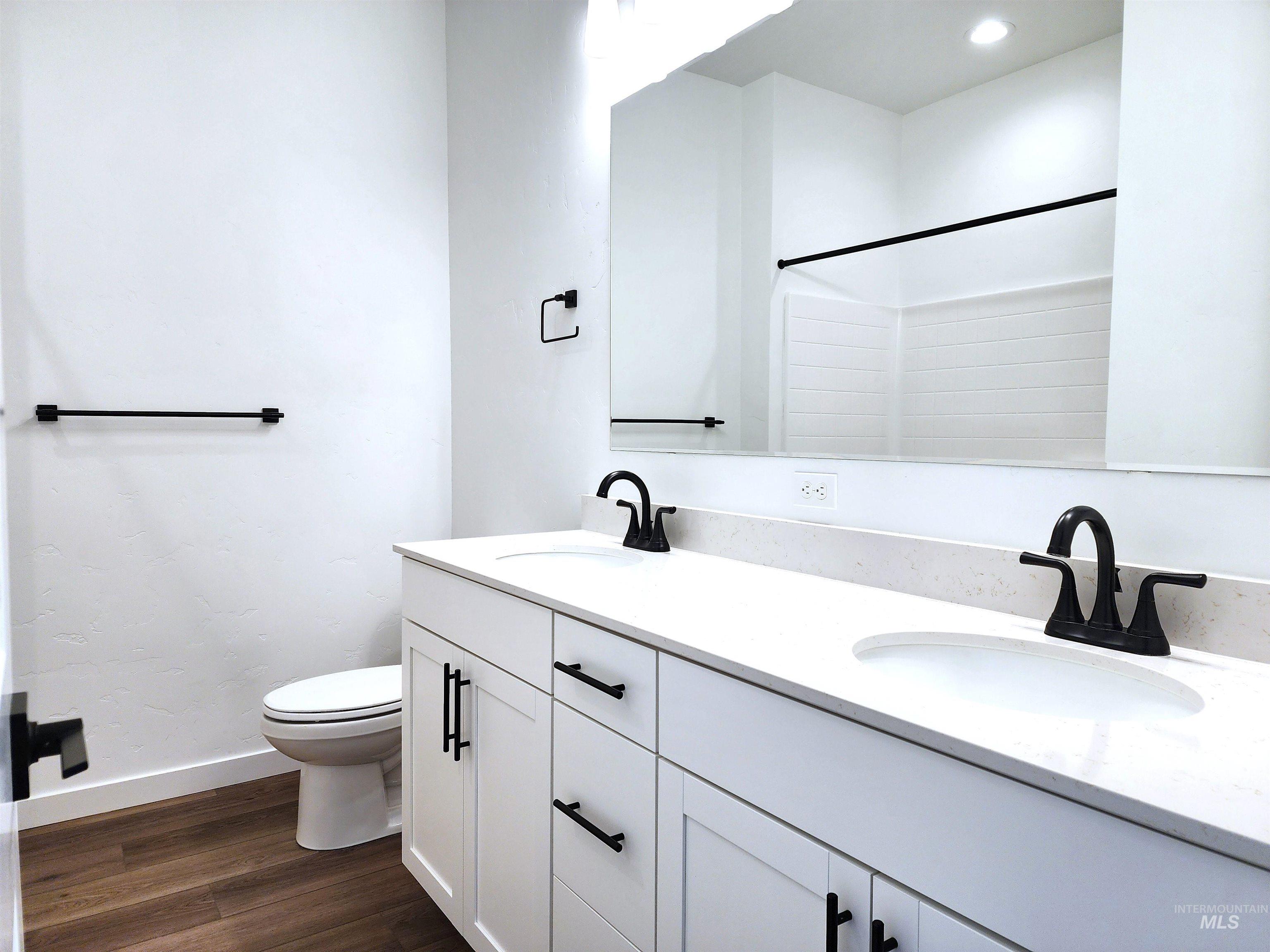 Bathroom with double vanity, dark wood-style floors, and a shower