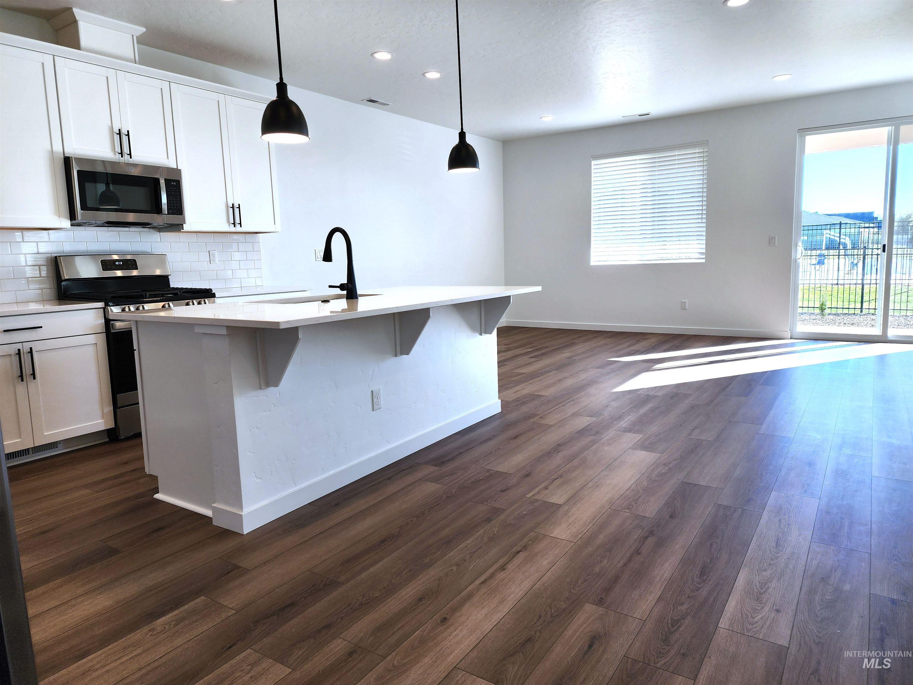 Kitchen with appliances with stainless steel finishes, tasteful backsplash, open floor plan, pendant lighting, and white cabinets
