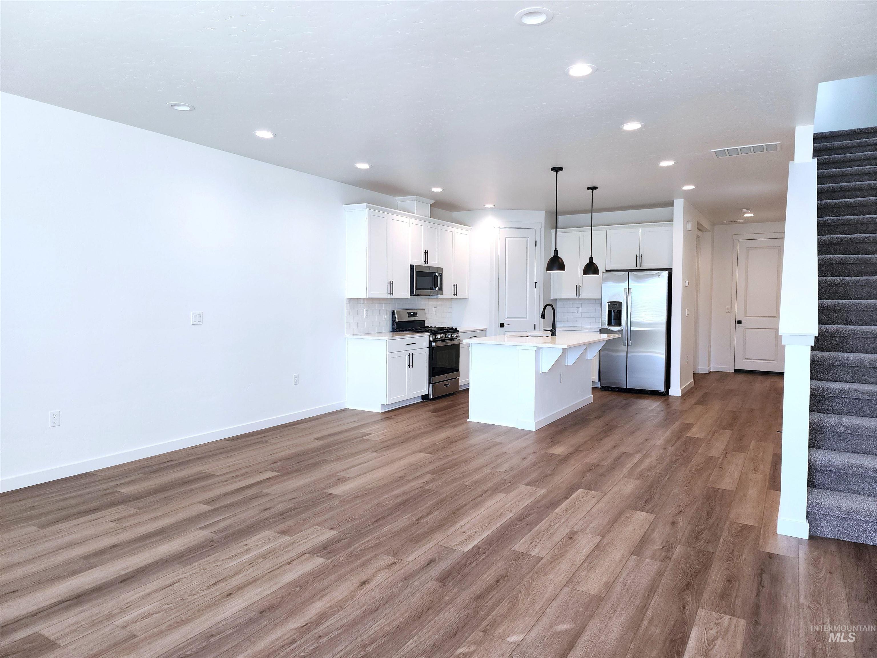 Kitchen featuring appliances with stainless steel finishes, white cabinetry, light wood finished floors, hanging light fixtures, and a breakfast bar