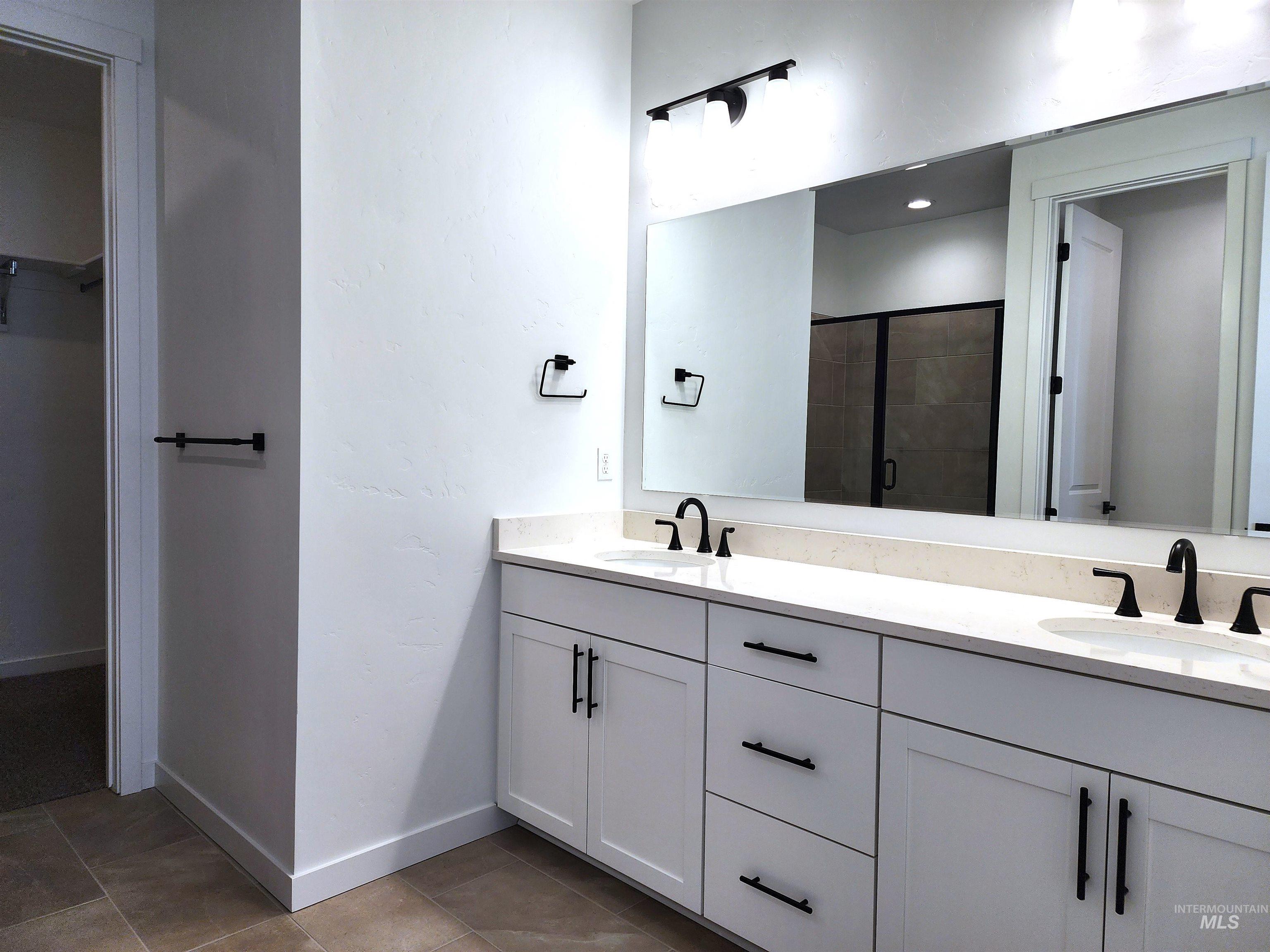 Full bathroom with a walk in closet, double vanity, a shower stall, and light tile patterned floors