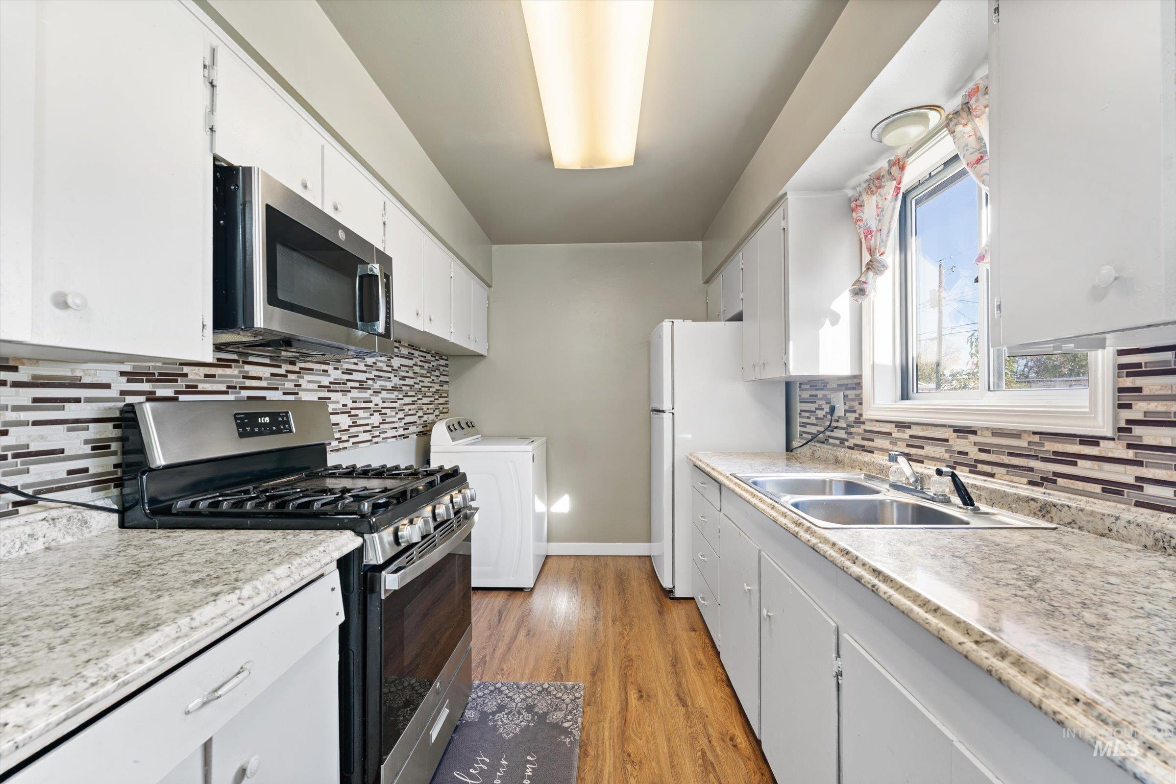 Kitchen with appliances with stainless steel finishes, washer / dryer, white cabinets, and light wood finished floors