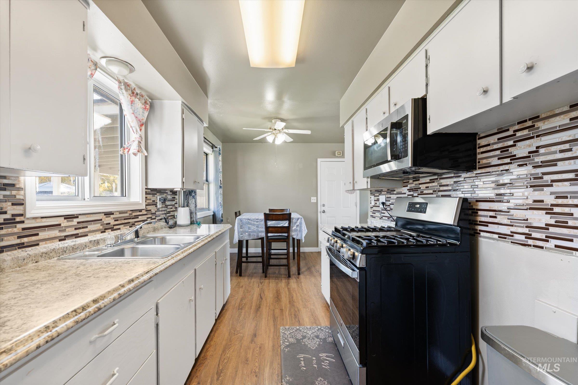 Kitchen with decorative backsplash, appliances with stainless steel finishes, white cabinetry, and light countertops