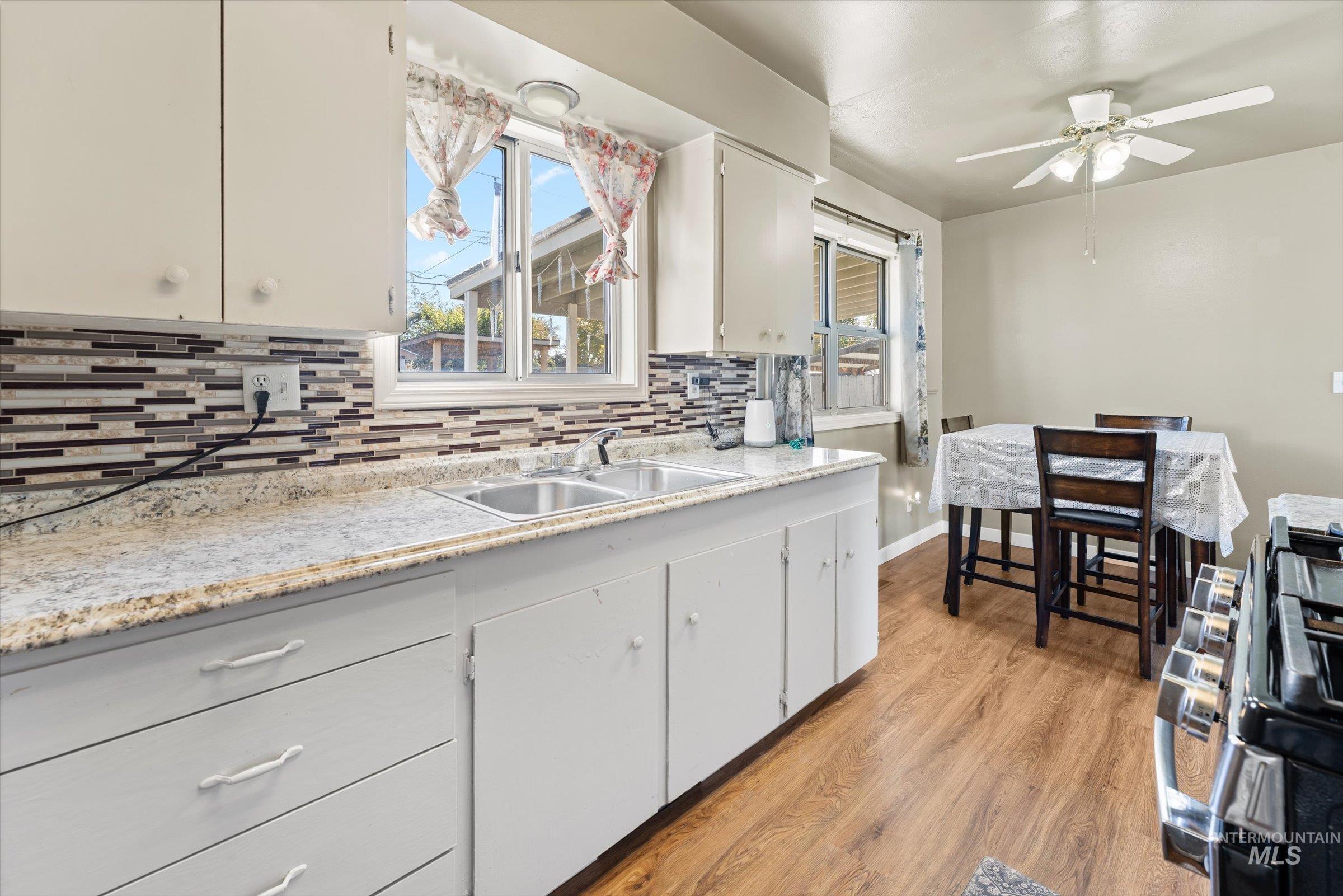 Kitchen featuring gas stove, light wood-type flooring, white cabinets, decorative backsplash, and a ceiling fan