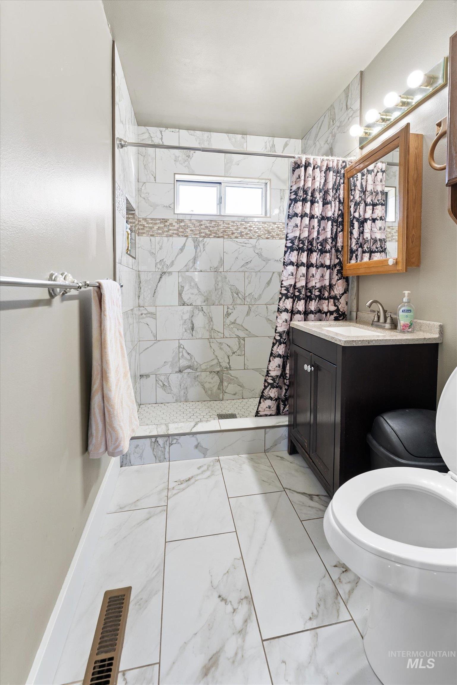 Bathroom featuring light marble finish flooring, a stall shower, and vanity