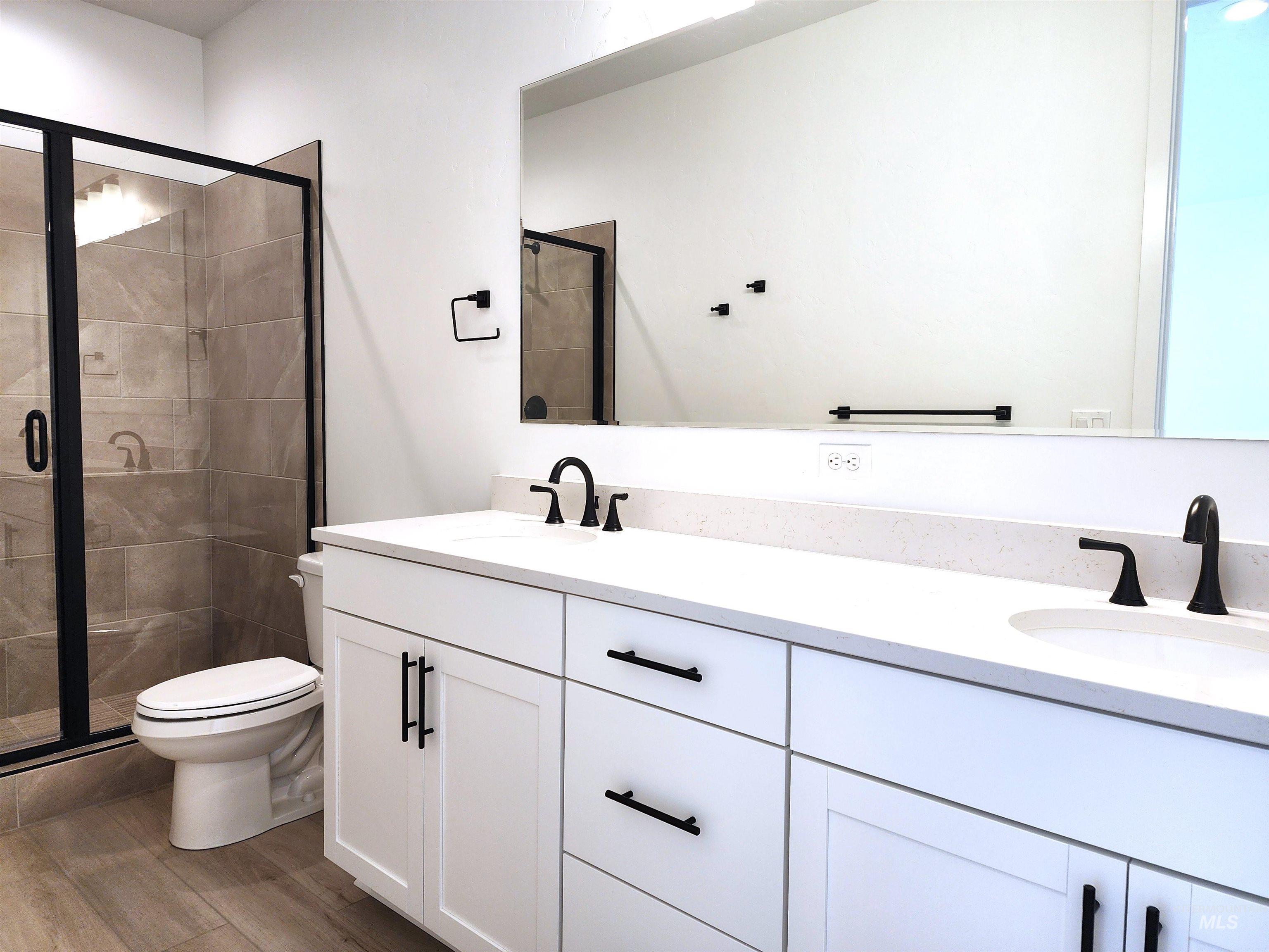 Full bath featuring a stall shower, double vanity, and light wood-style flooring