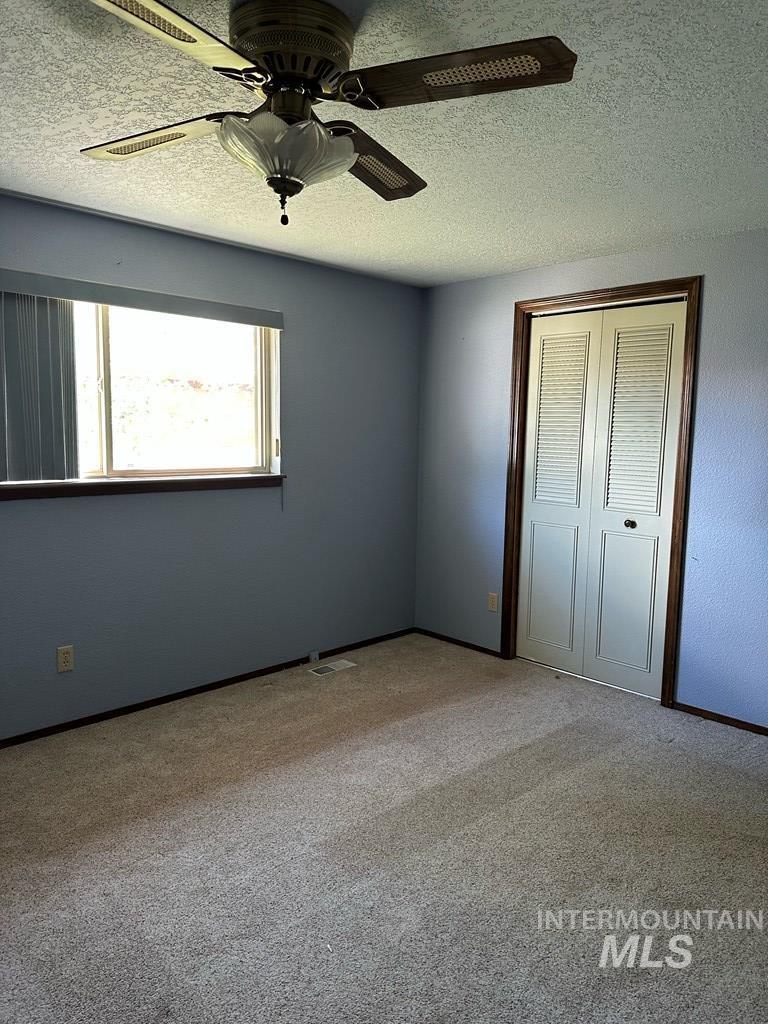 Unfurnished bedroom featuring a closet, a textured ceiling, light colored carpet, and ceiling fan