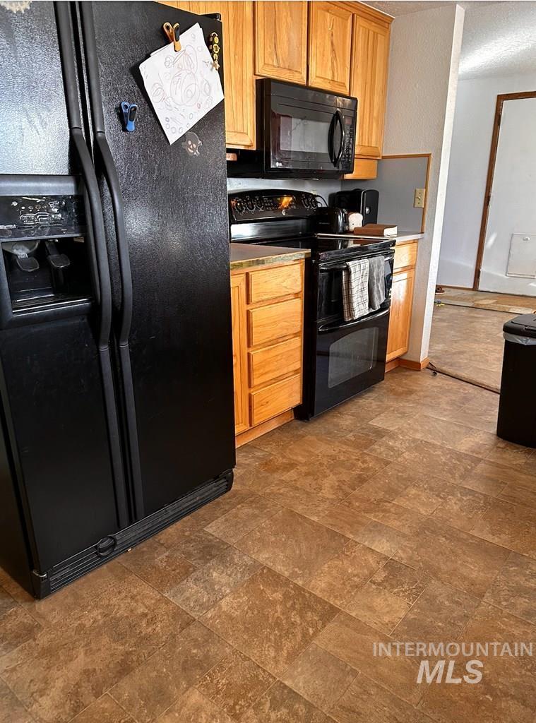 Kitchen featuring black appliances, stone finish flooring, and brown cabinetry