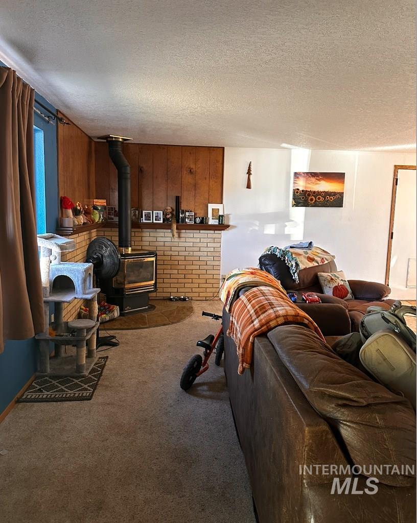 Carpeted living area with a wood stove, a textured ceiling, and wooden walls
