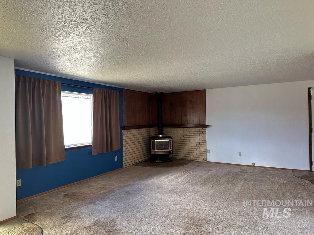 Unfurnished living room with a wood stove, carpet flooring, and a textured ceiling