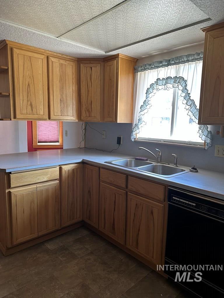 Kitchen with light countertops, black dishwasher, open shelves, brown cabinets, and dark stone finish flooring