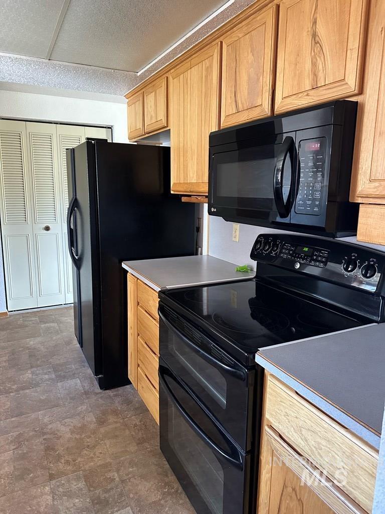 Kitchen with black appliances, stone finish flooring, a textured ceiling, light brown cabinetry, and light countertops