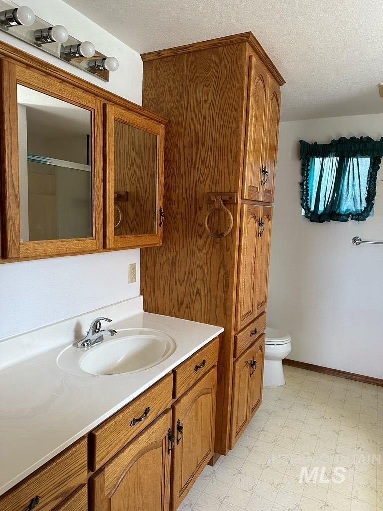 Full bathroom featuring vanity, light floors, a shower with door, and a textured ceiling