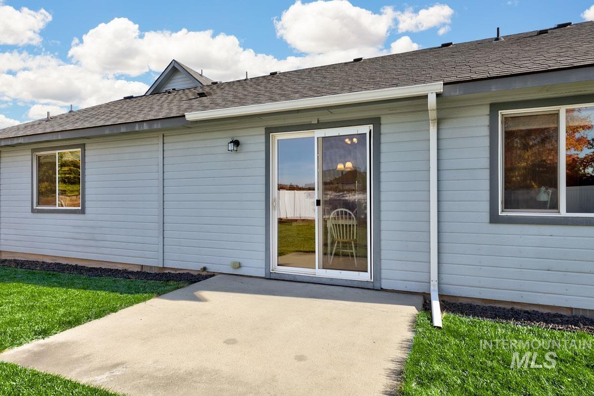 Entrance to property featuring a patio area, a shingled roof, and a lawn